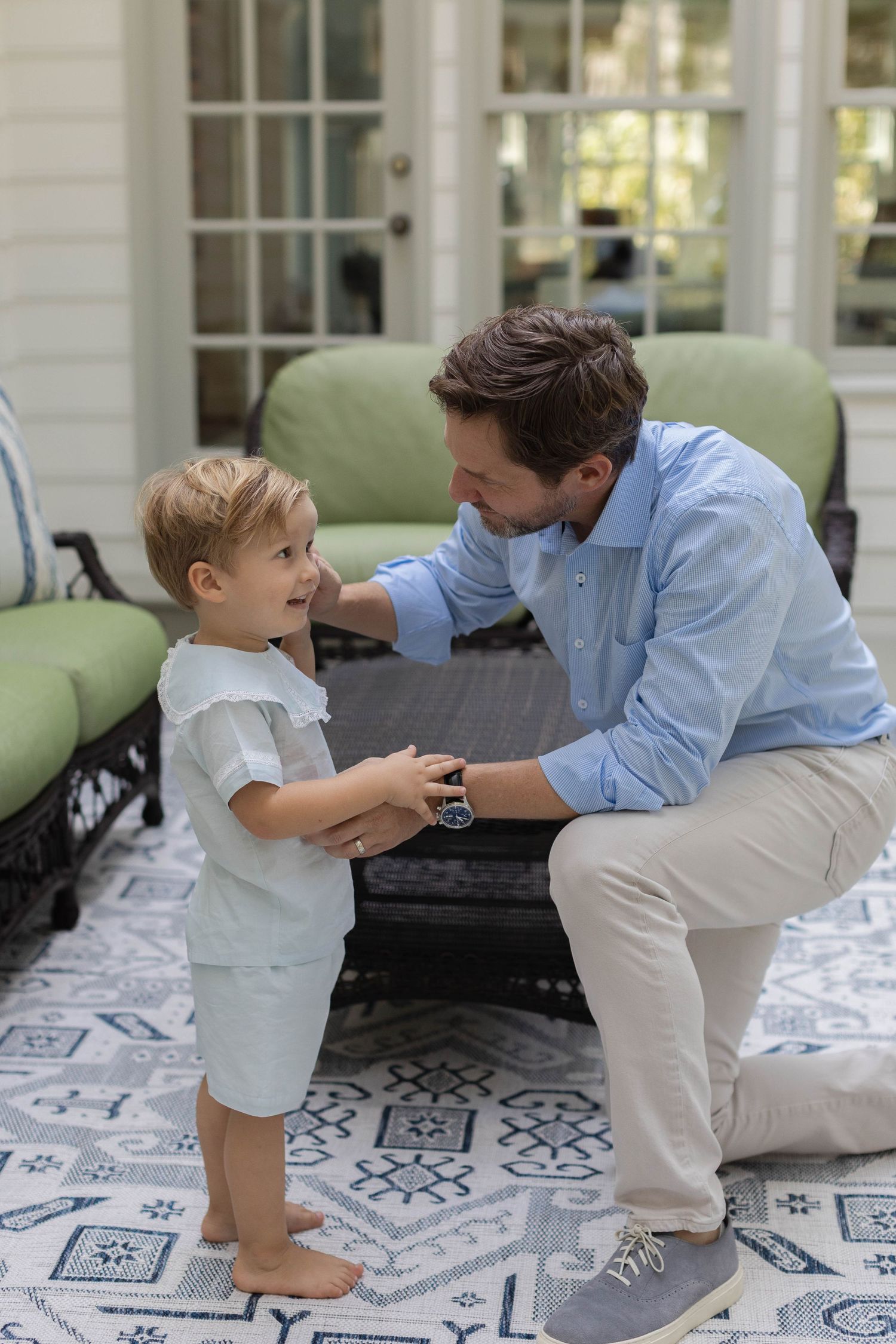 Family bonding moment showing playful interaction on a patterned porch with green cushioned furniture.