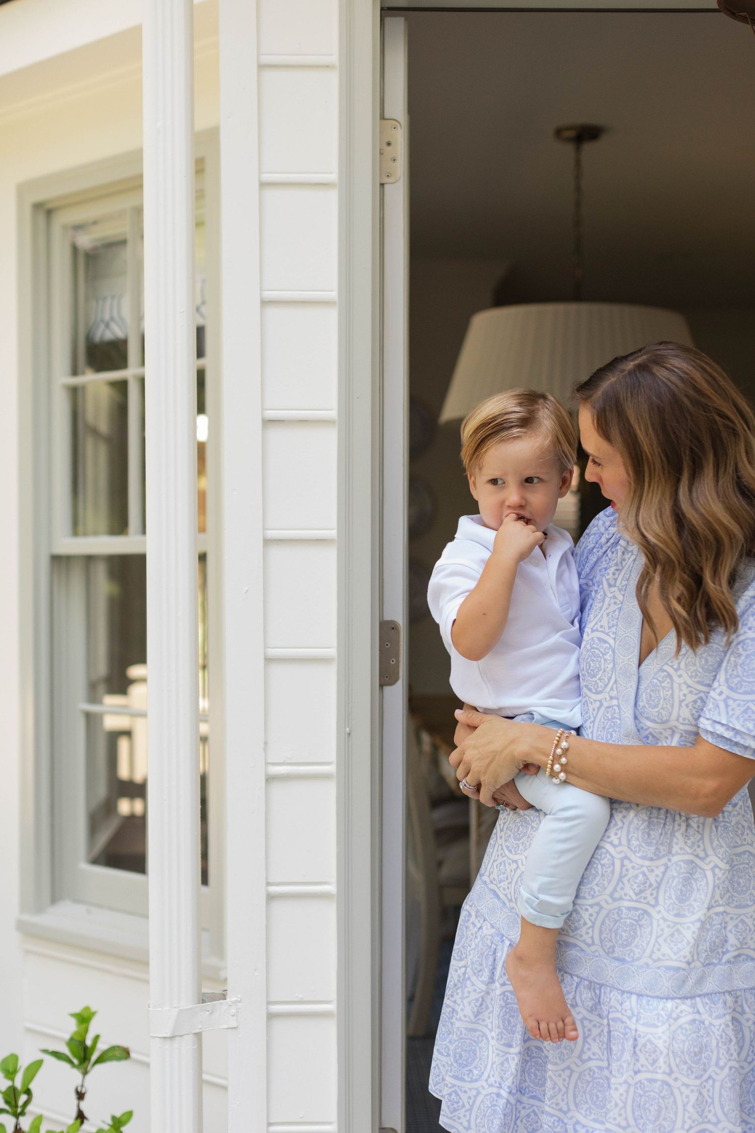 Family dressed in light blue and white sits on front porch steps of white house with coordinating outfits.
