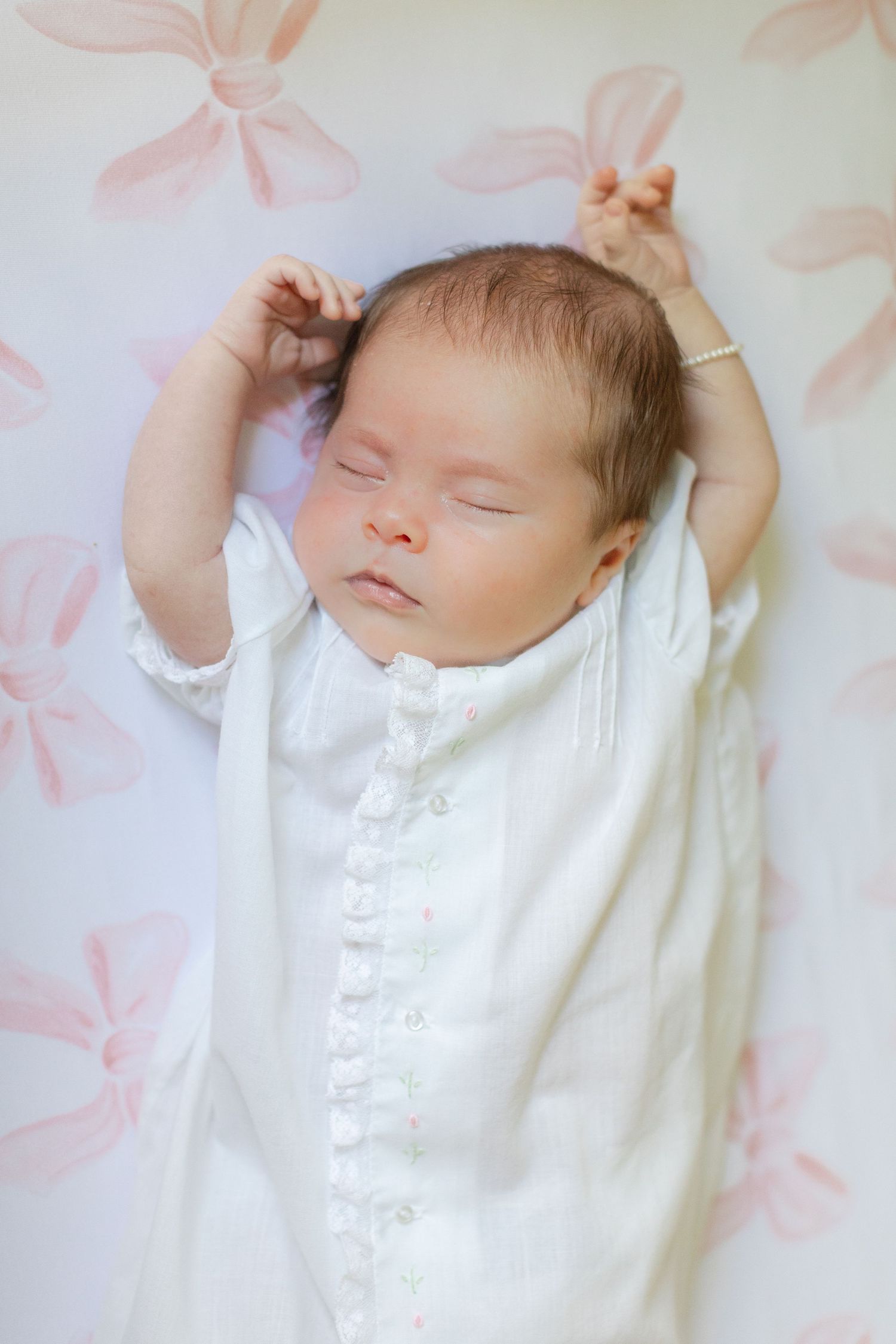 Peaceful newborn baby sleeping in white button-up outfit on floral pink and white blanket.