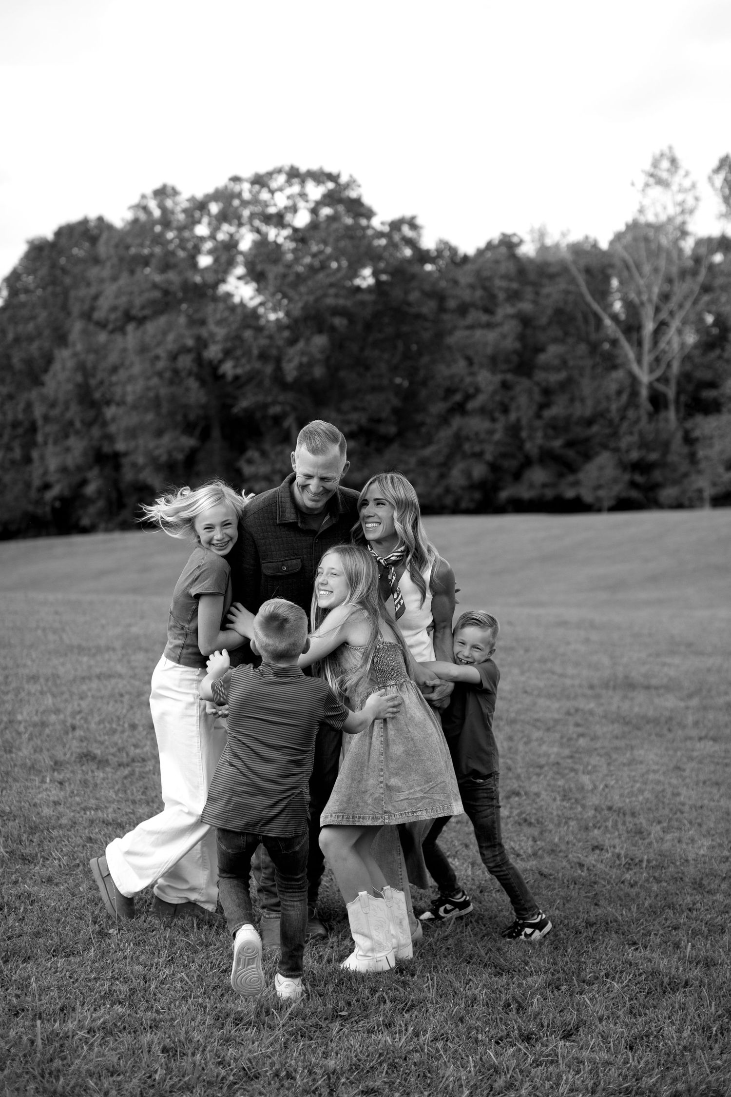 A sequence of black and white photos showing a family playing and hugging together in a grassy field.