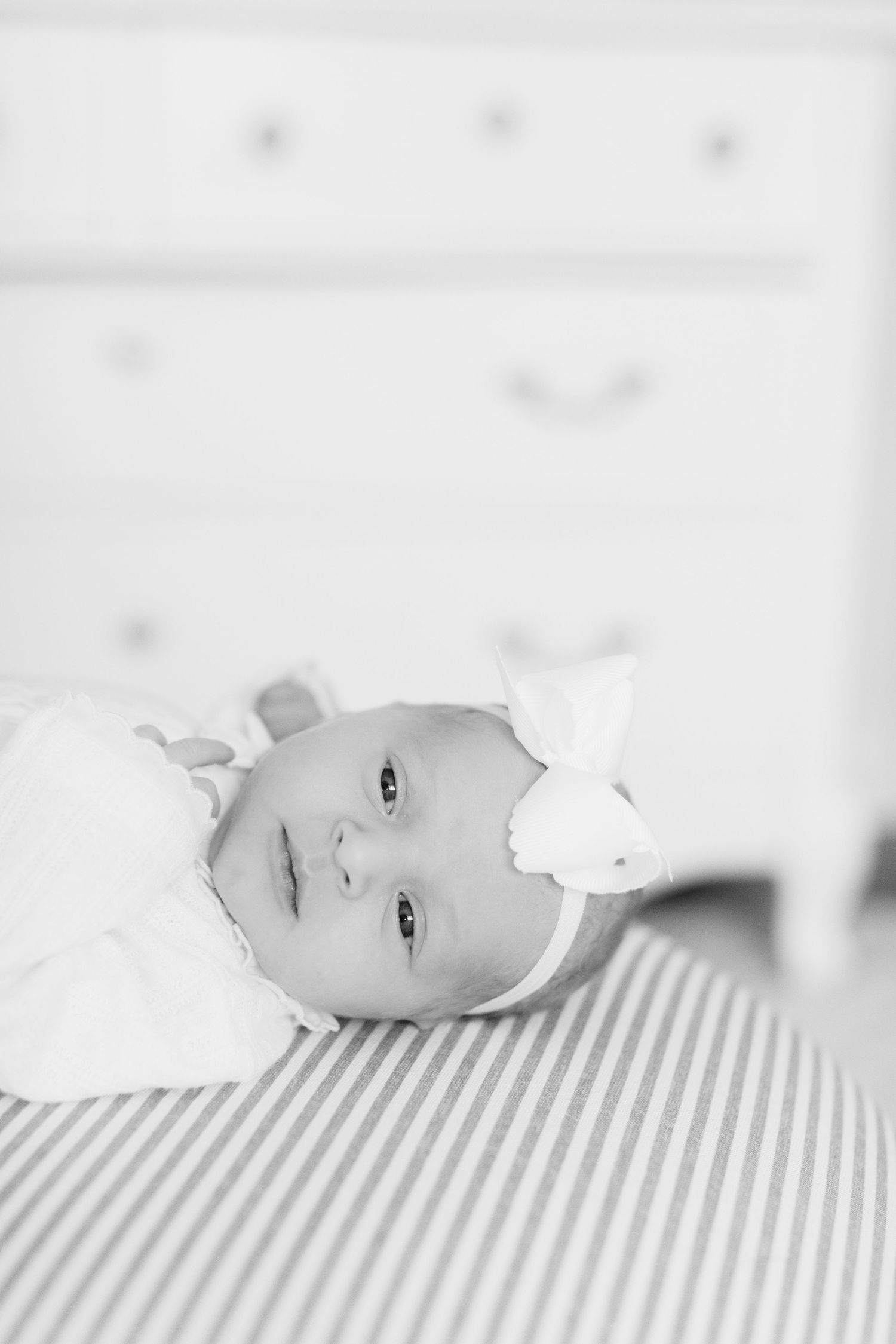 Black and white portrait of an infant lying on striped bedding.