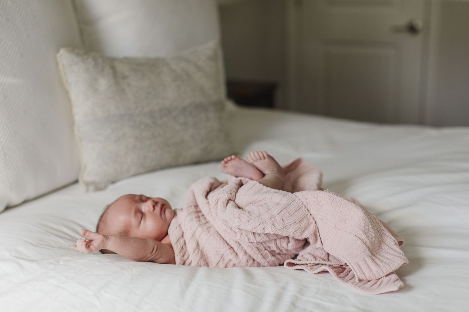 Sleeping newborn in pink outfit lying peacefully on white bedding.