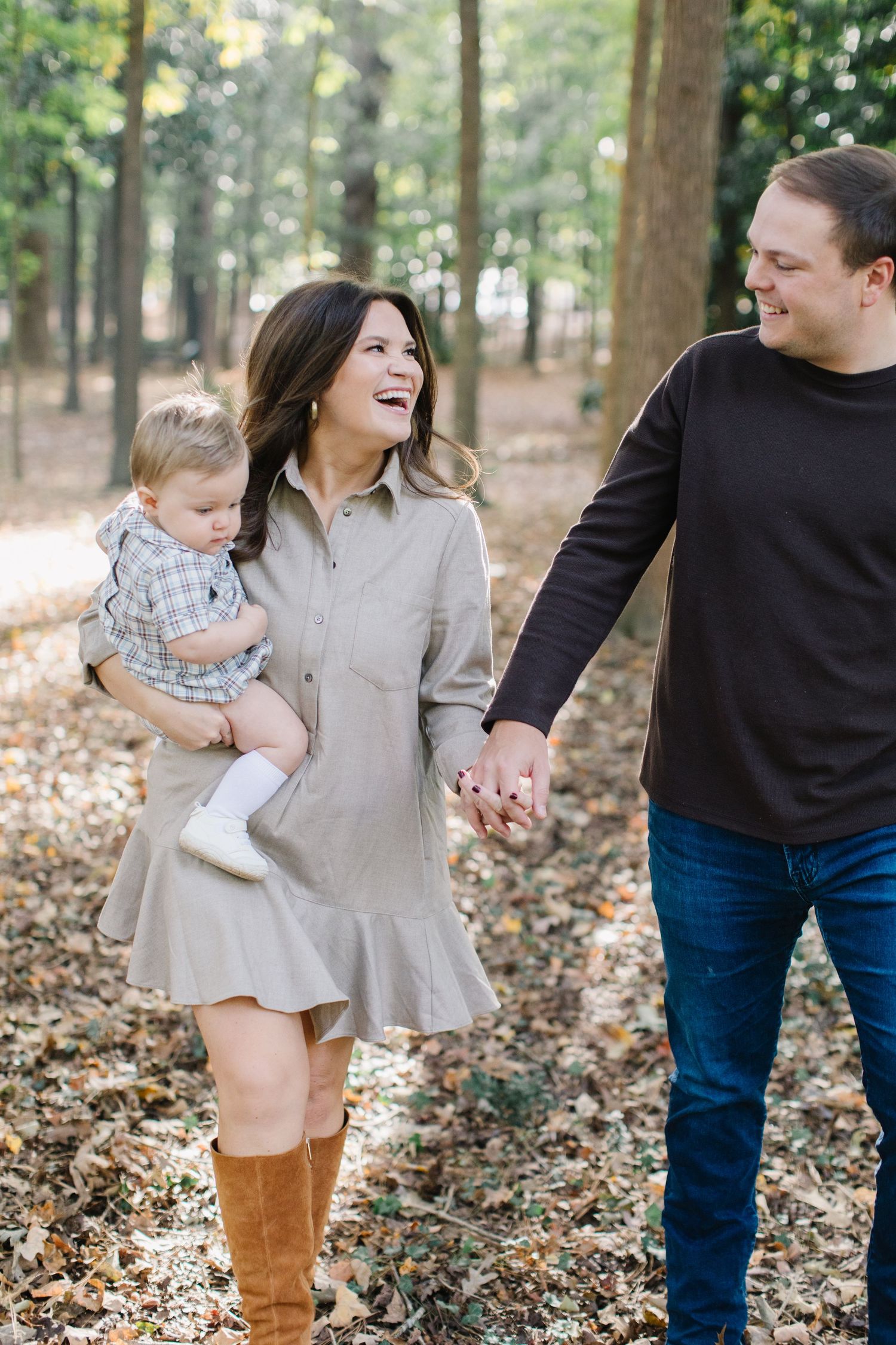 A family enjoys a playful autumn moment together in a wooded area covered with fallen leaves.