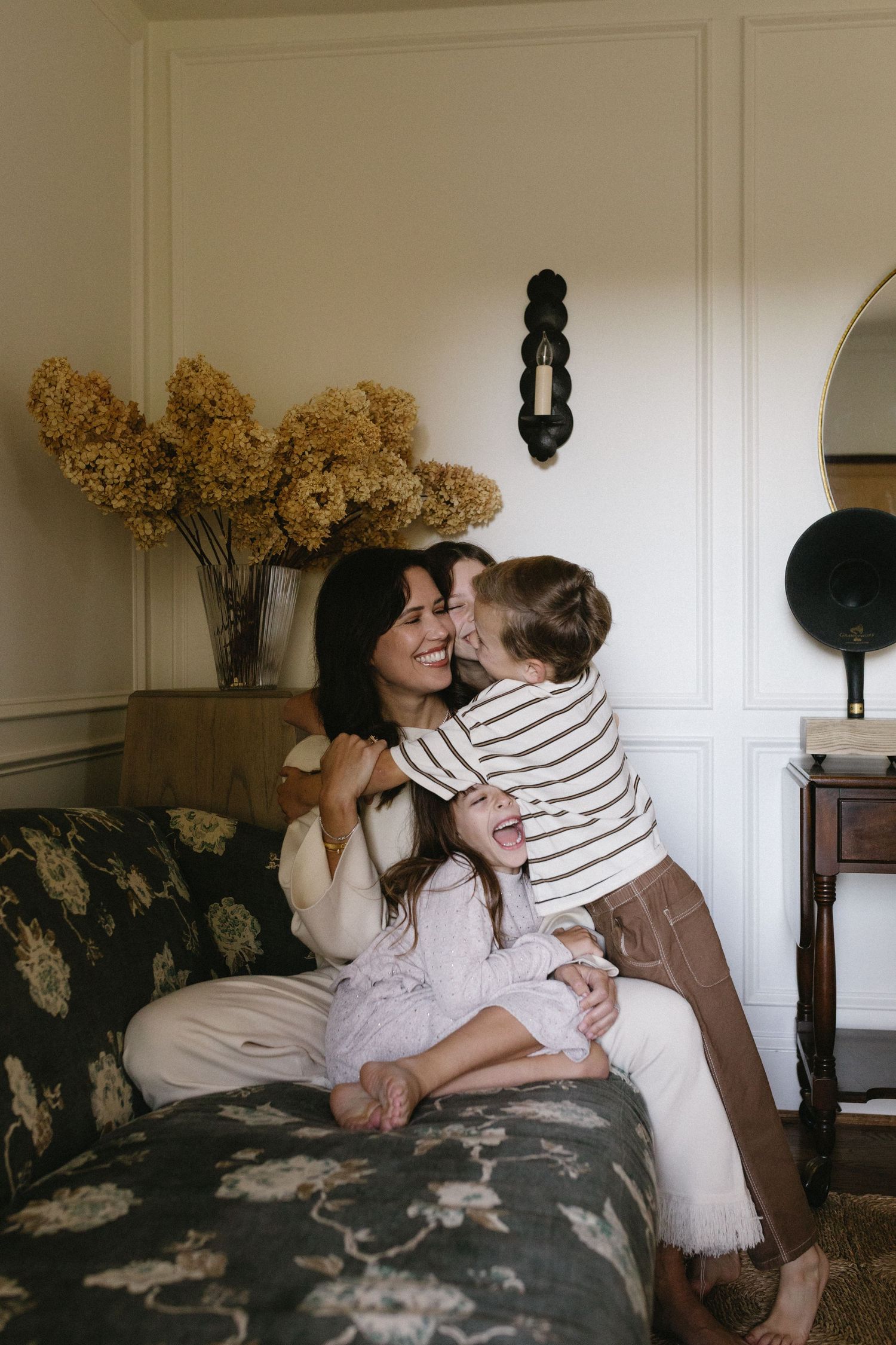 A cozy moment shared between family members on a floral patterned couch with dried hydrangeas in the background.