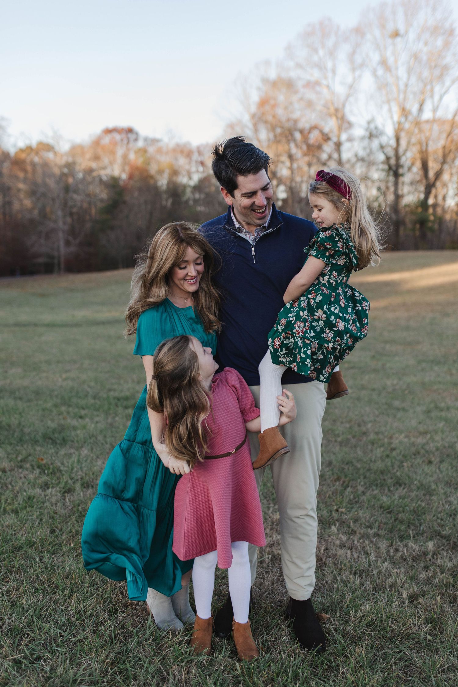 A family in coordinating green and pink outfits shares joyful moments together in a grassy field at sunset.
