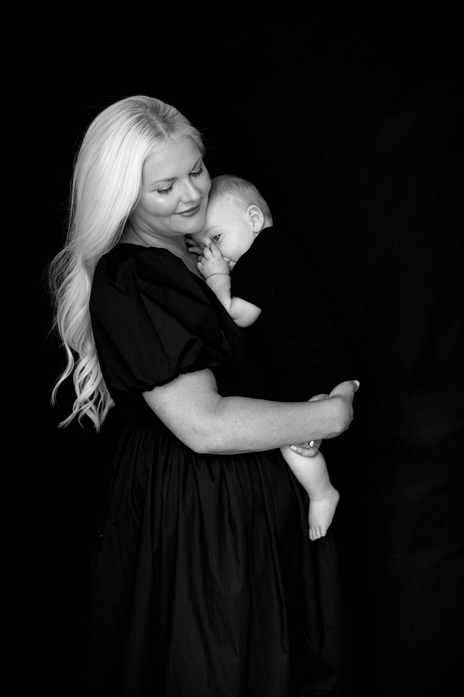 Intimate black and white portraits of mother and child embracing against dark background.