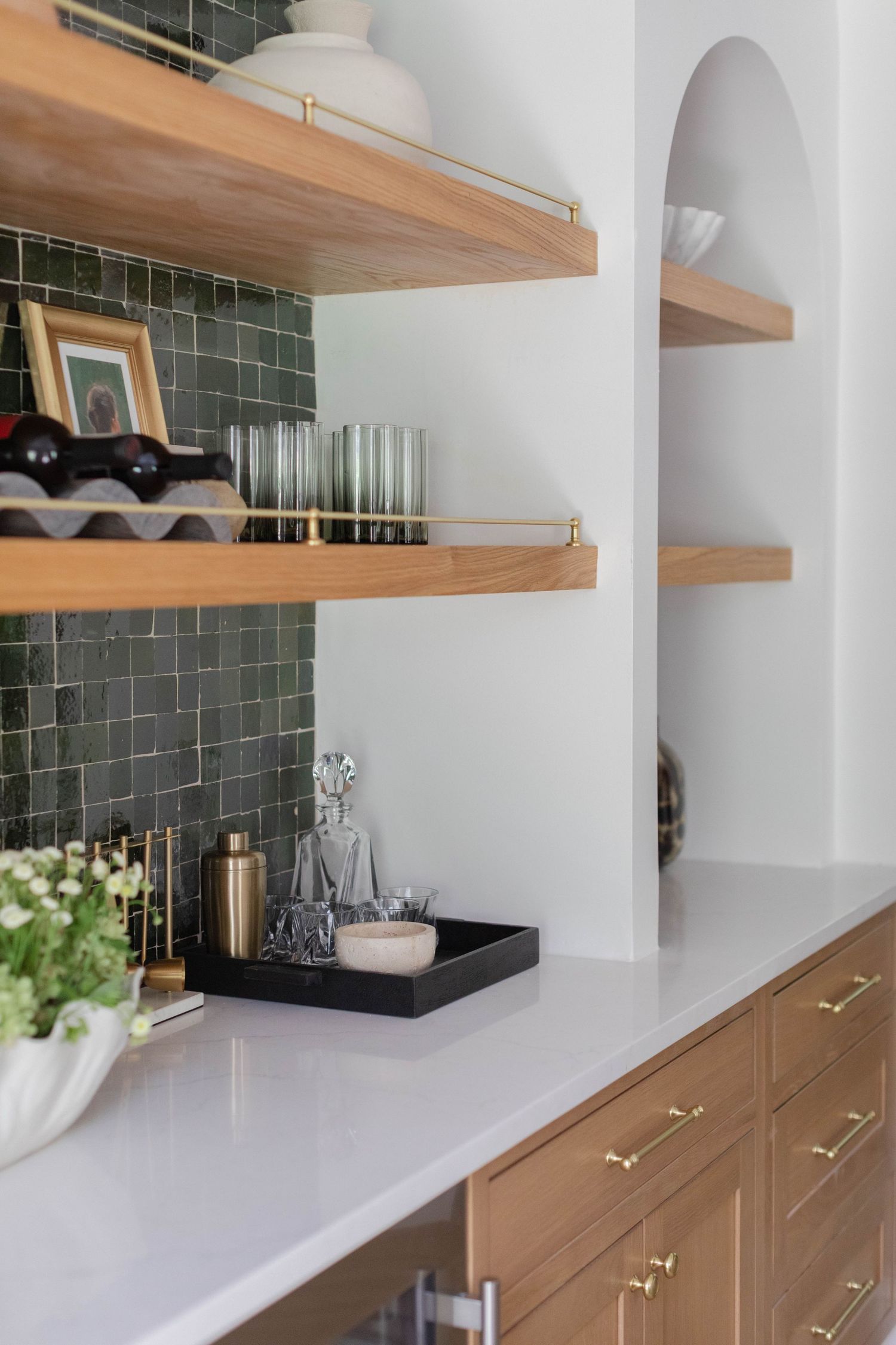 Modern kitchen with wooden open shelves, white countertop, green tile backsplash, and decorative items on display.