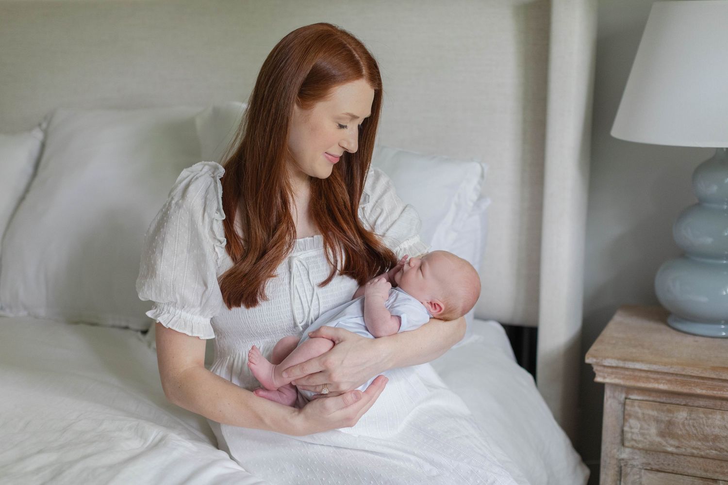Tender moment as parent cradles sleeping newborn baby in white bedding.
