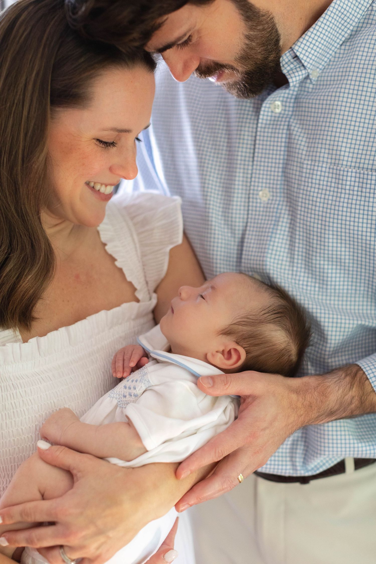 A family shares tender moments as they care for a newborn baby in warm natural lighting.