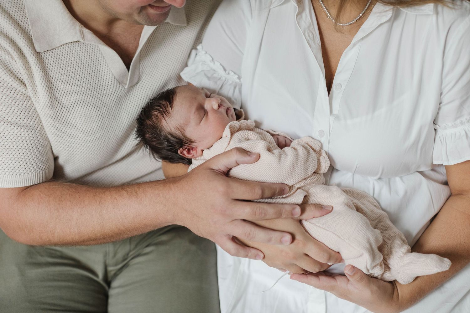 Parent and newborn sharing intimate moments in white outfits on a soft surface.
