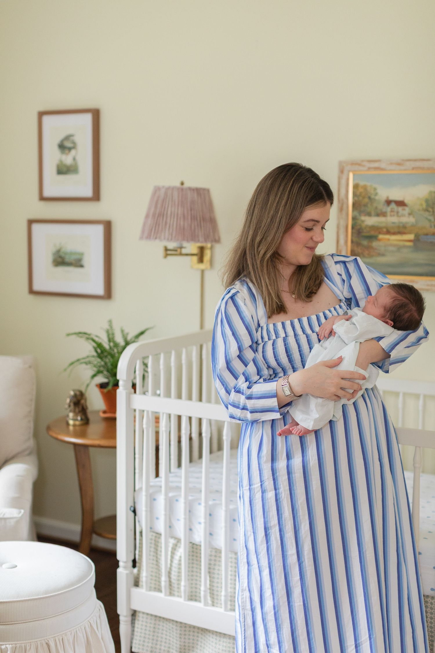 A series of tender moments in a nursery with blue and white striped clothing and a white crib against beige walls.
