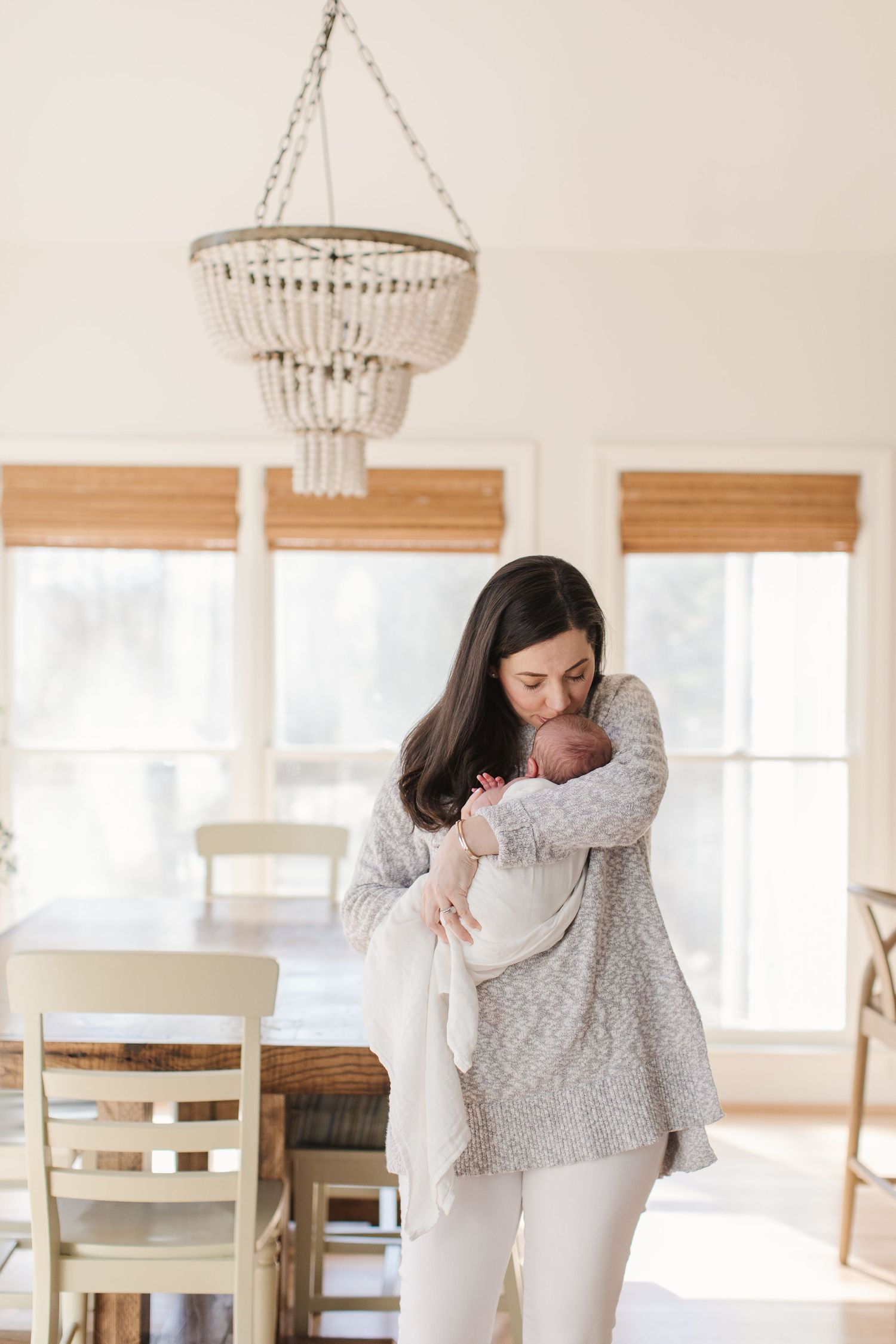 Family members share emotional embrace in bright room with hanging chandelier and bamboo shades.