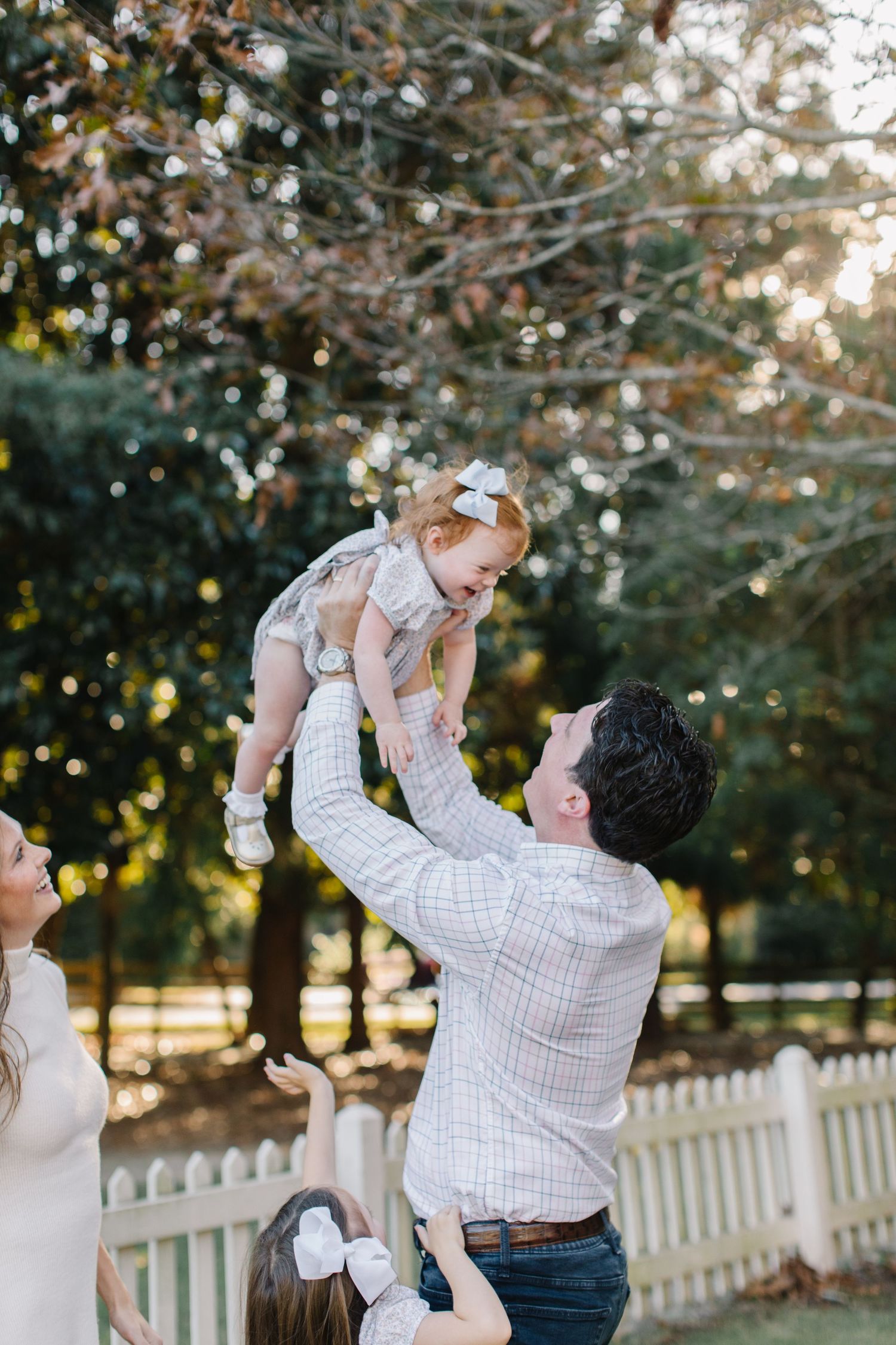 Joyful outdoor family moments captured against a white picket fence at sunset.