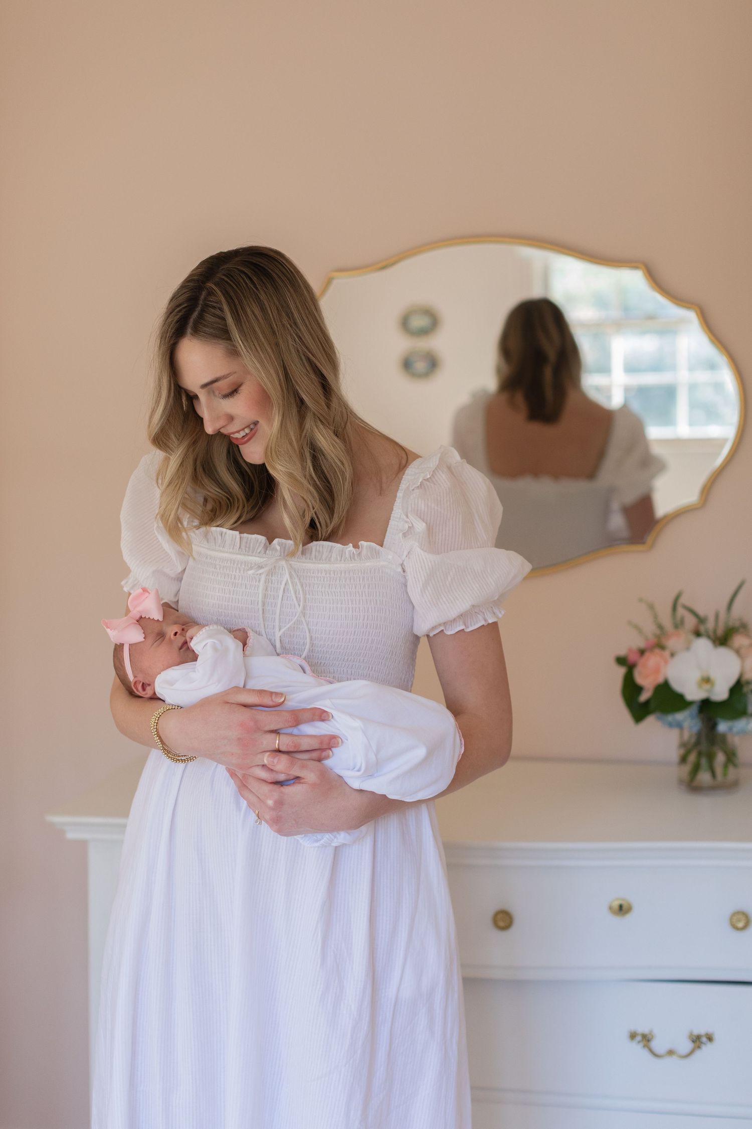 A woman in a white dress holds a newborn baby in a series of gentle poses.