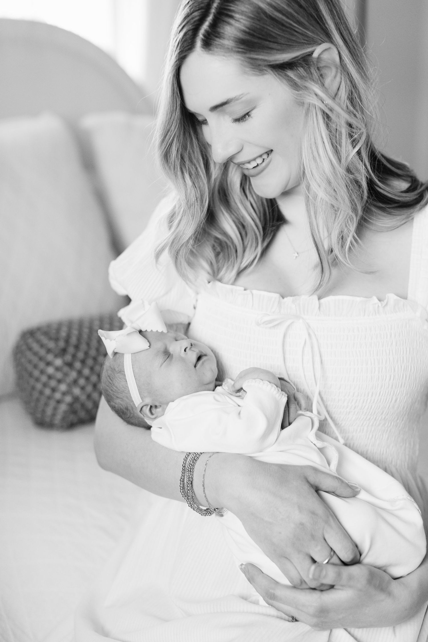 A tender black and white portrait of a parent cradling a newborn baby in a white outfit.