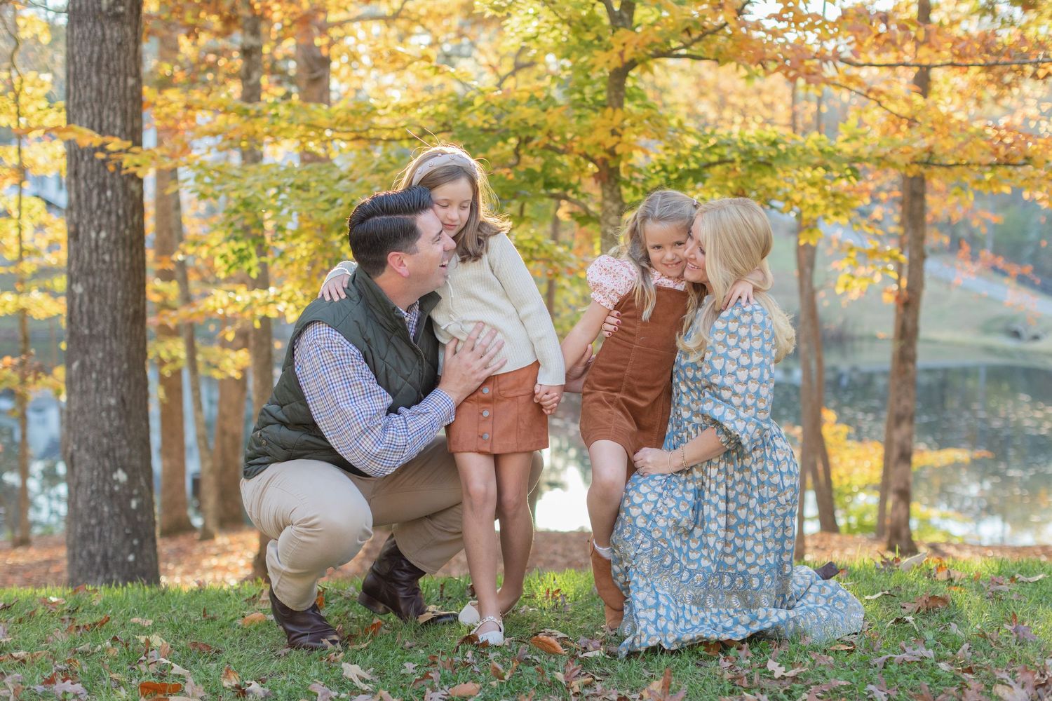 A family enjoys a tender moment together in an autumn forest setting with golden foliage in the background.