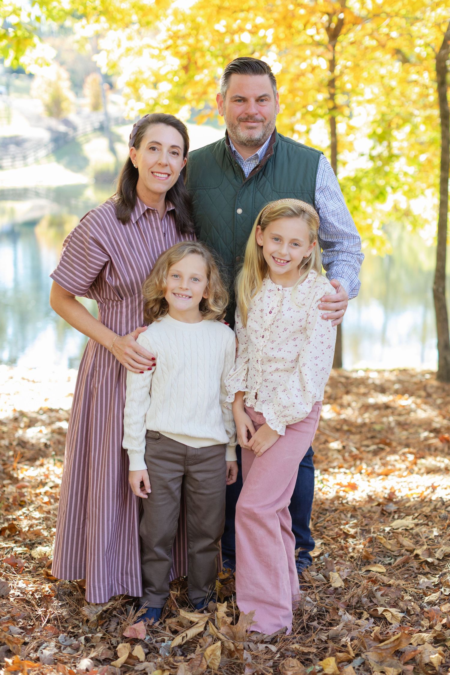 Family poses together in autumn forest with golden leaves and warm sunlight filtering through trees.