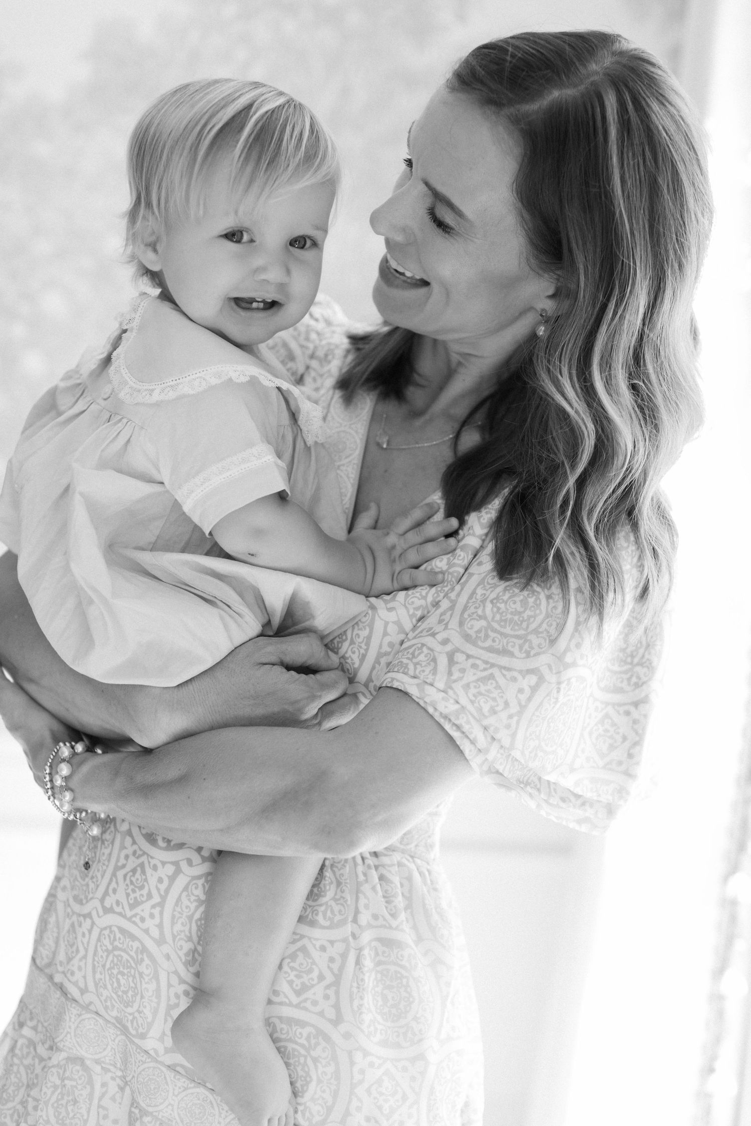 A sweet series of black and white photos showing tender moments between mother and baby in matching white outfits.
