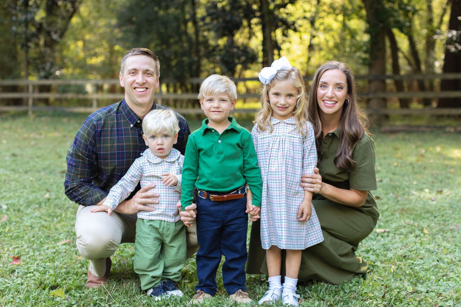 A family sits together on grass during an outdoor autumn photoshoot in a park setting.