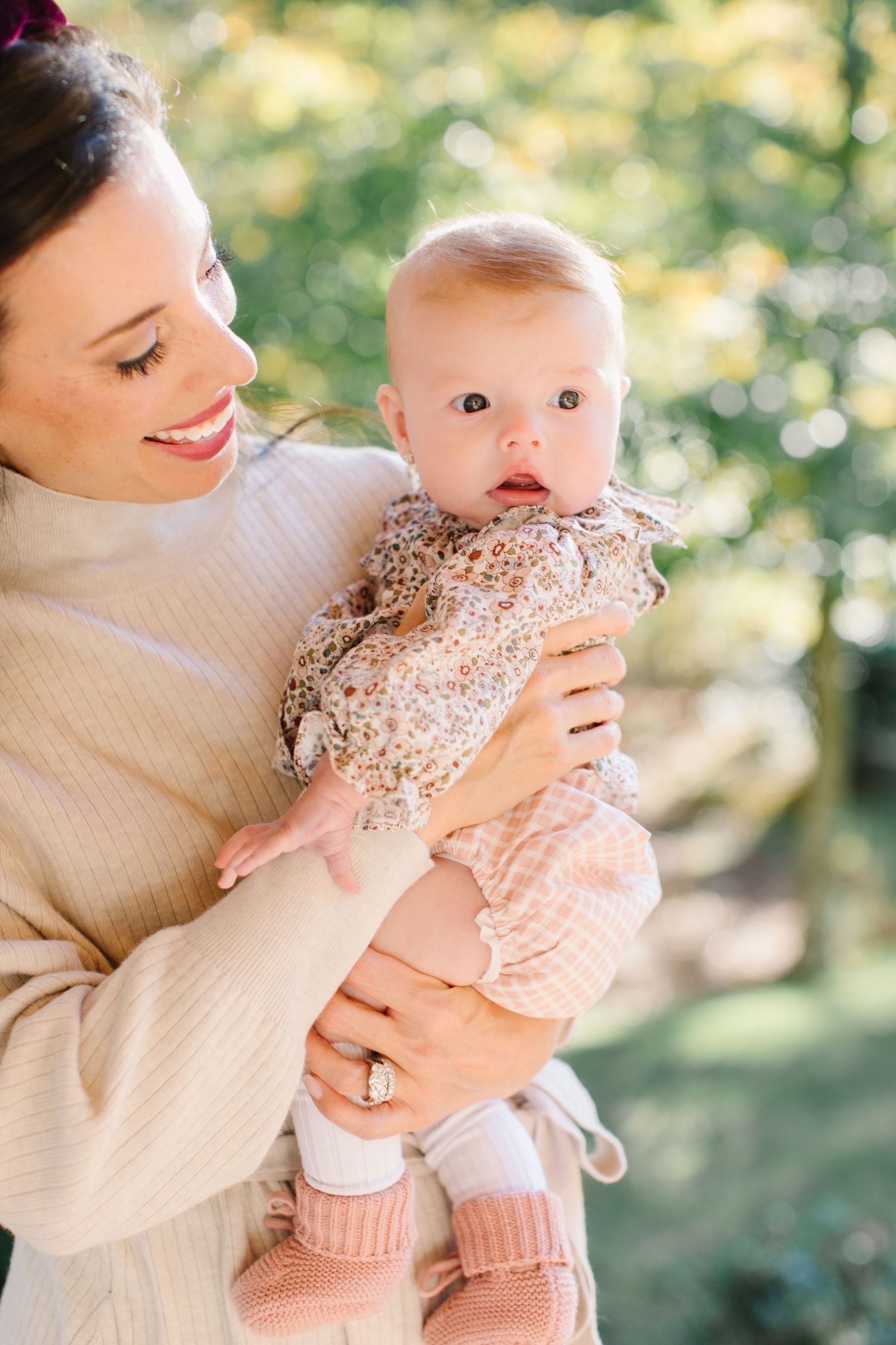 A baby in a floral dress and pink pants is held lovingly outdoors in a series of sweet candid moments.