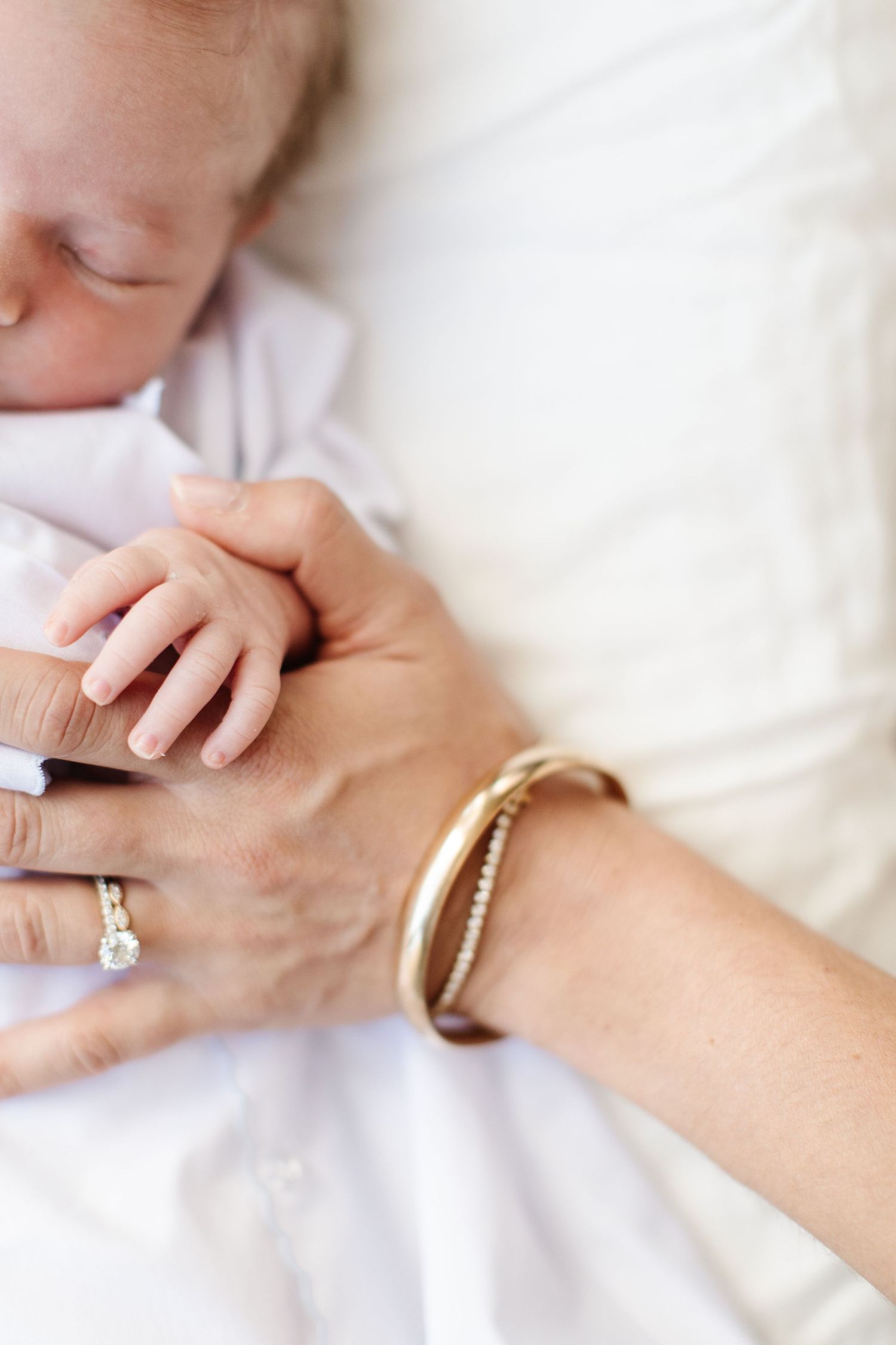 Close-up of hands with engagement ring and bracelet against white fabric background.