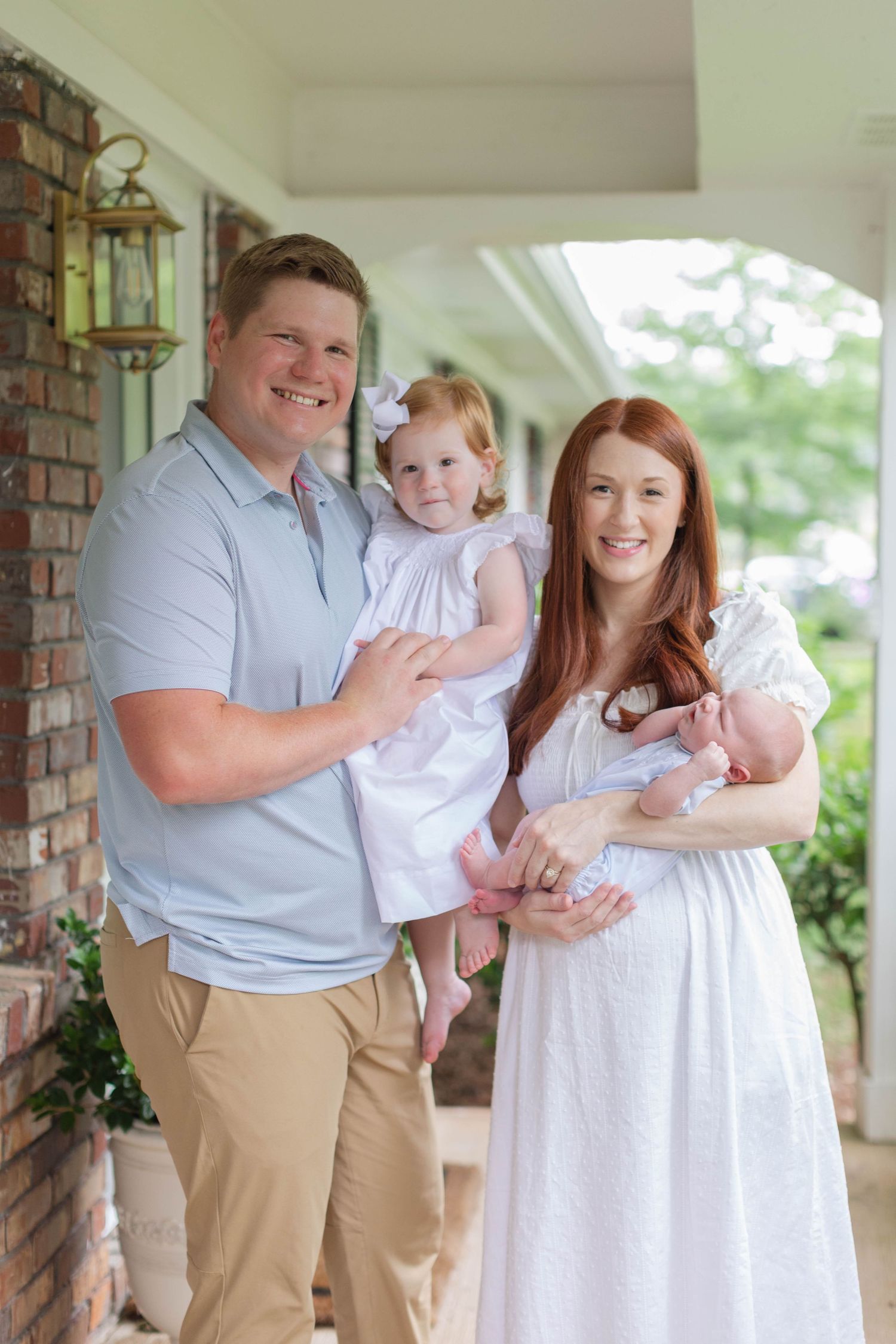 Family portrait session on a covered porch with brick columns and natural lighting.