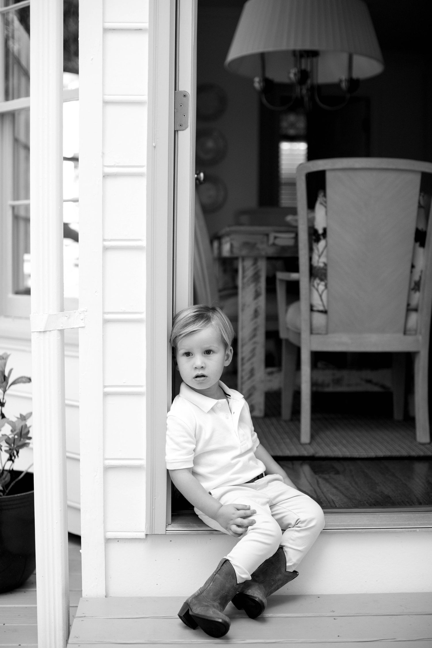 Three black and white portraits of toddler sitting on white front porch in casual wear.
