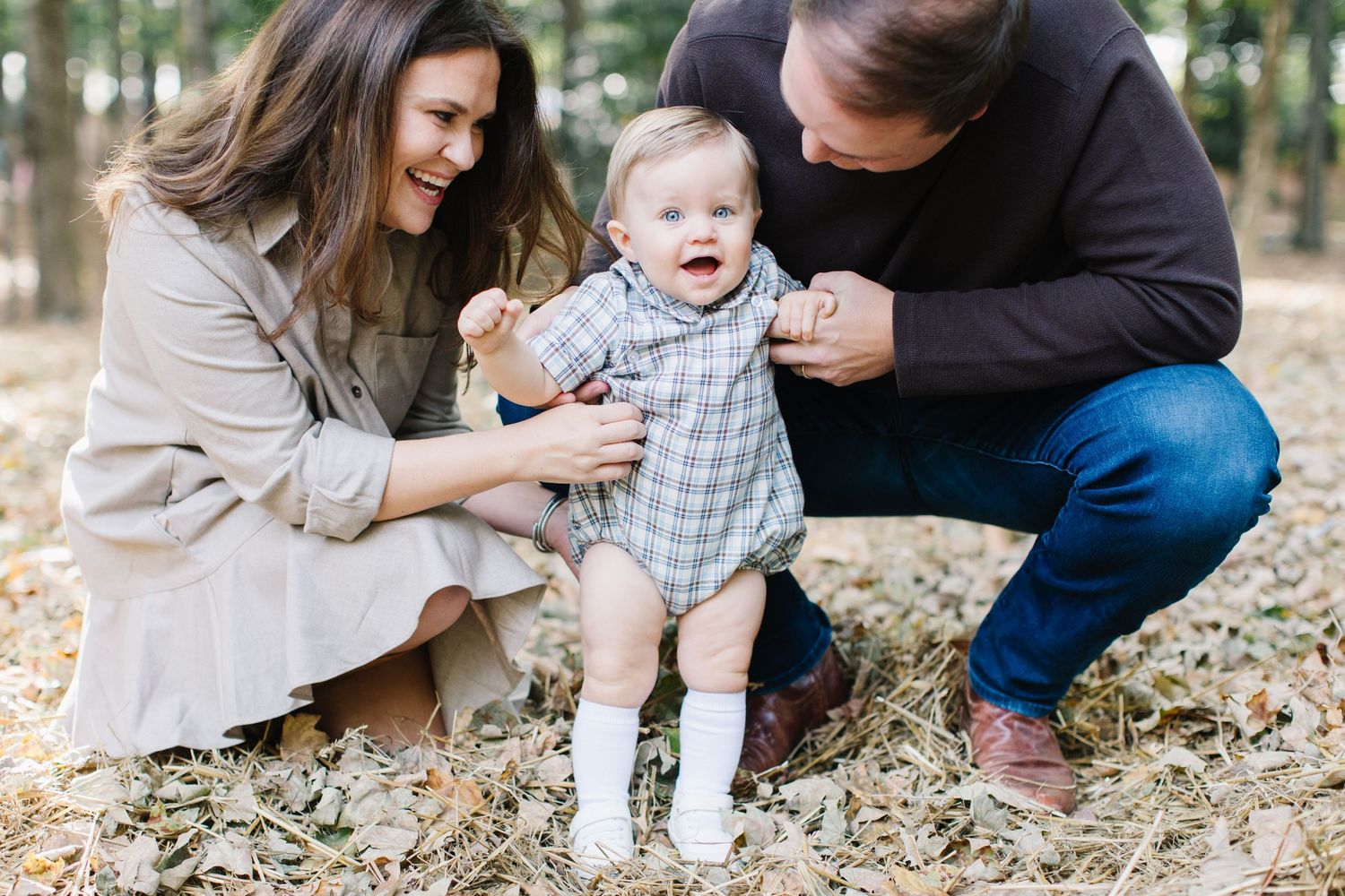 Family plays together in fallen autumn leaves during outdoor photo session in wooded area.
