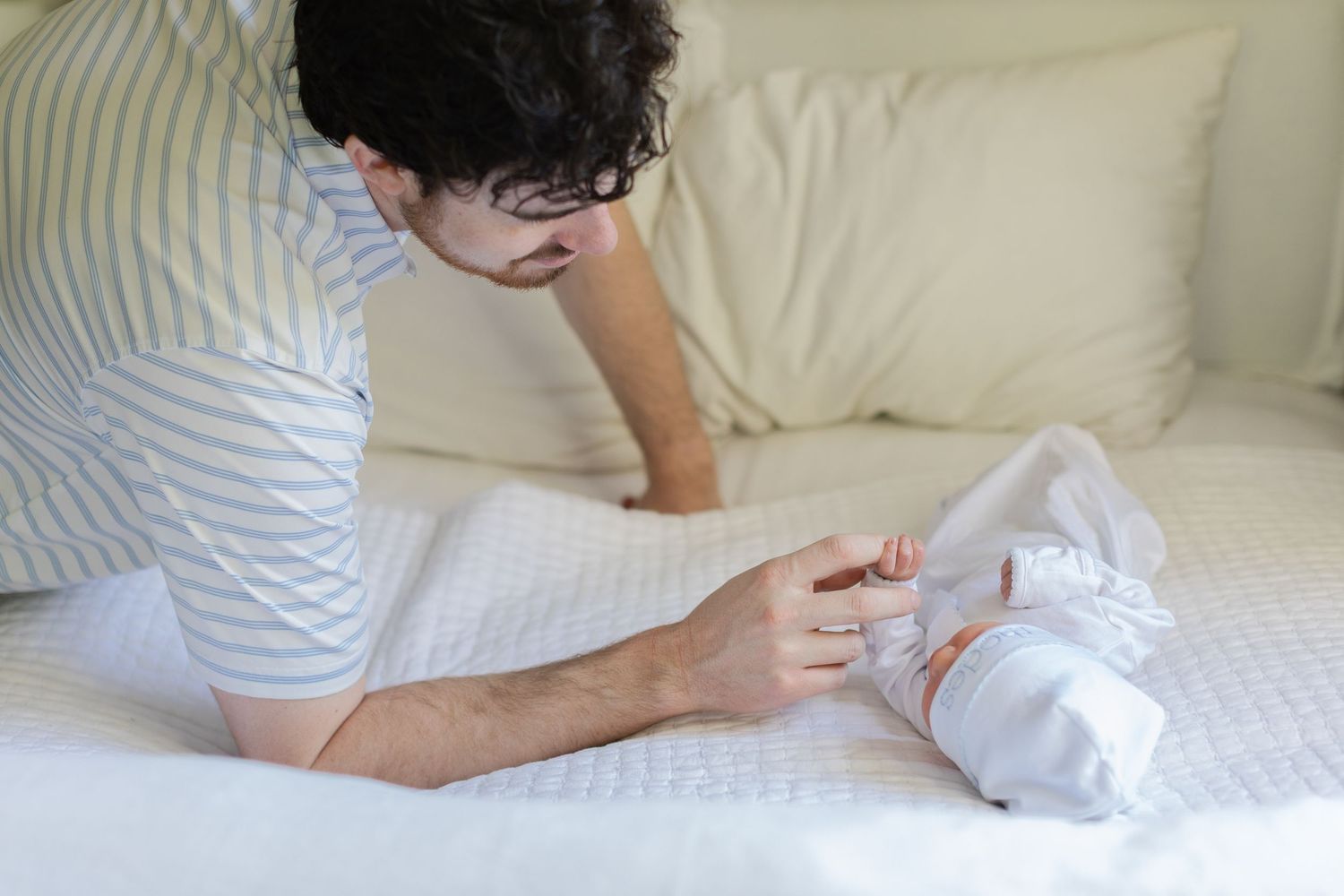 Father tenderly caring for newborn baby on white bed, bonding moment between dad and infant.