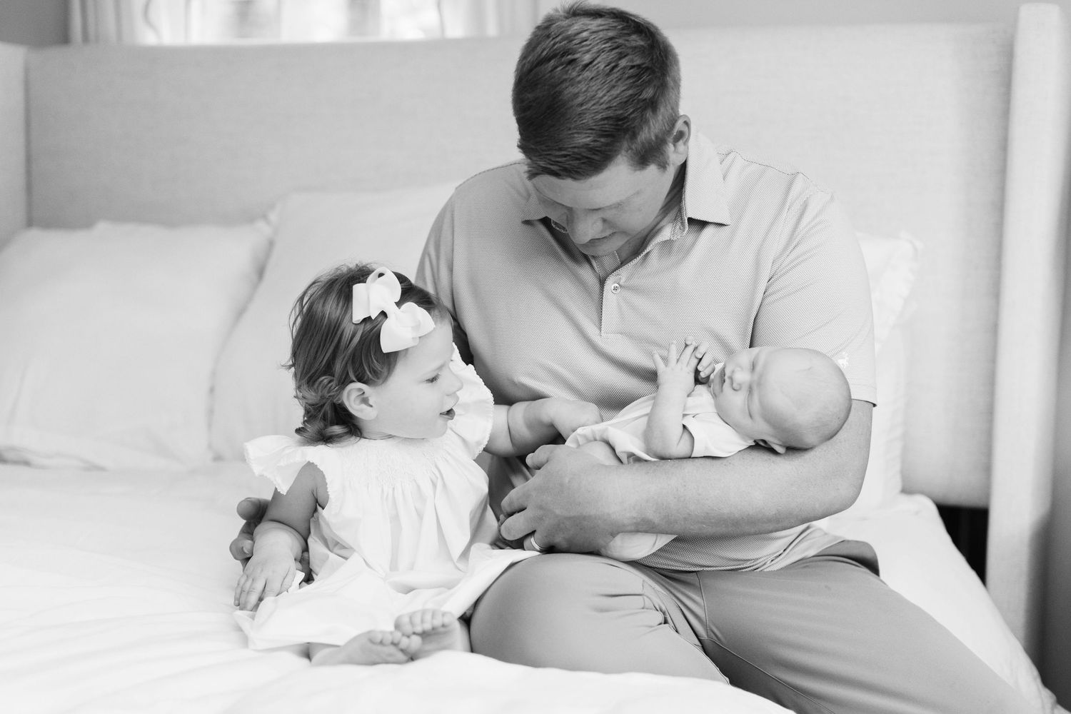 Natural newborn photography session featuring tender moments and gentle touches on white bedding.