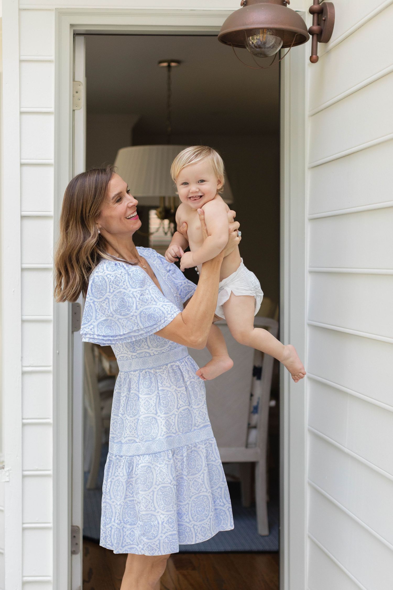 Mother and baby share joyful moments on a white porch while wearing coordinating blue floral outfits.