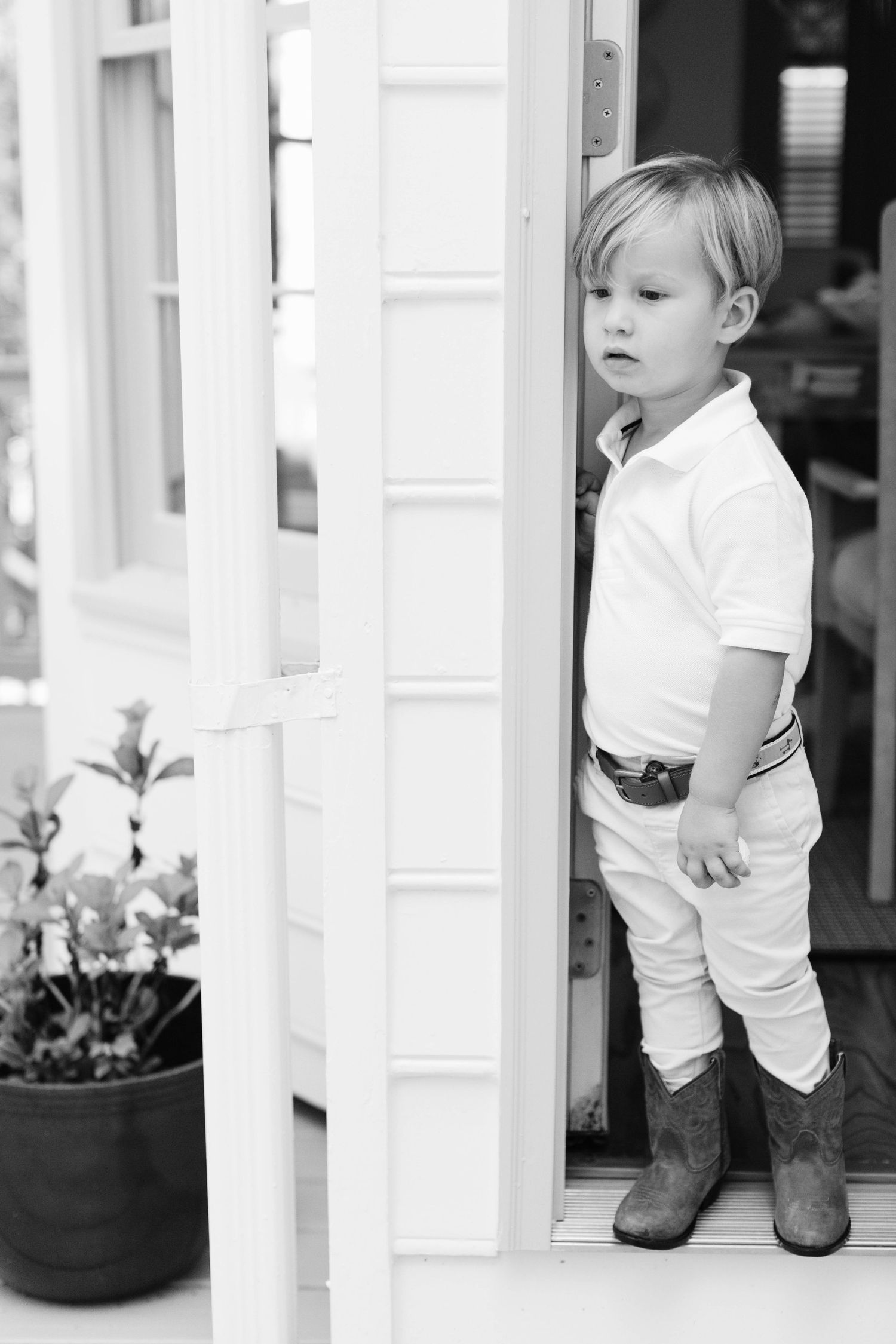 Black and white photo series showing a small child in white clothing and boots standing between porch columns.