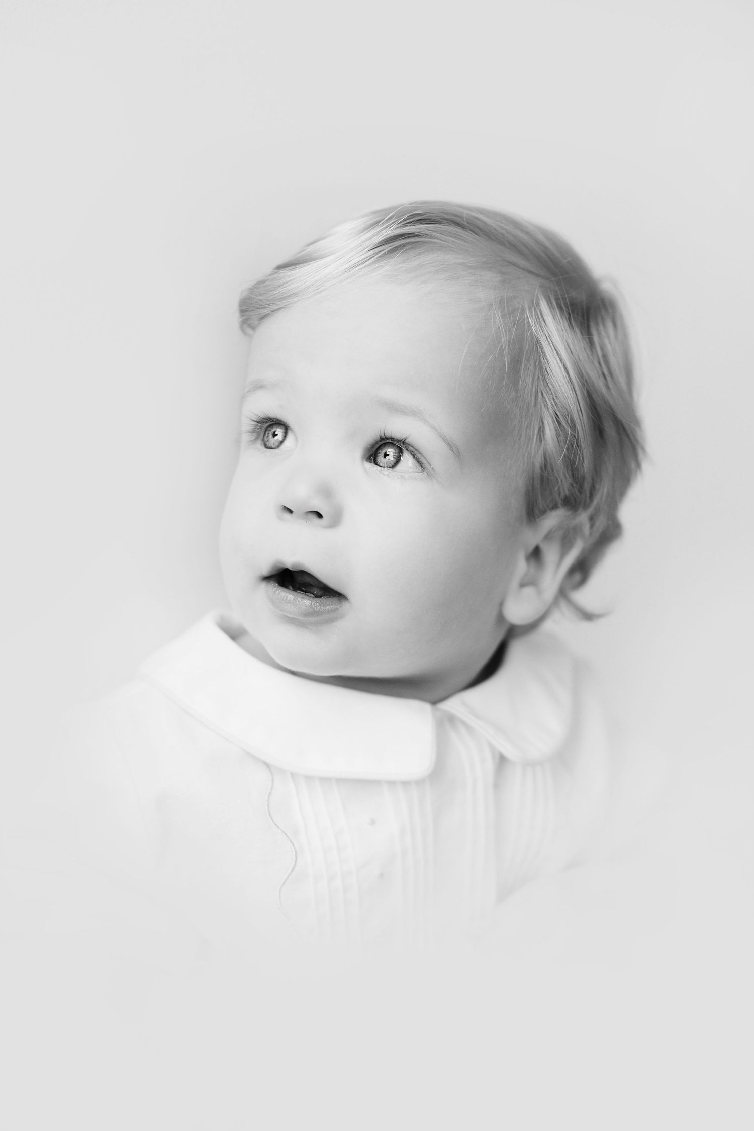 A black and white artistic triptych showing a baby's face from different angles looking upward with soft lighting.