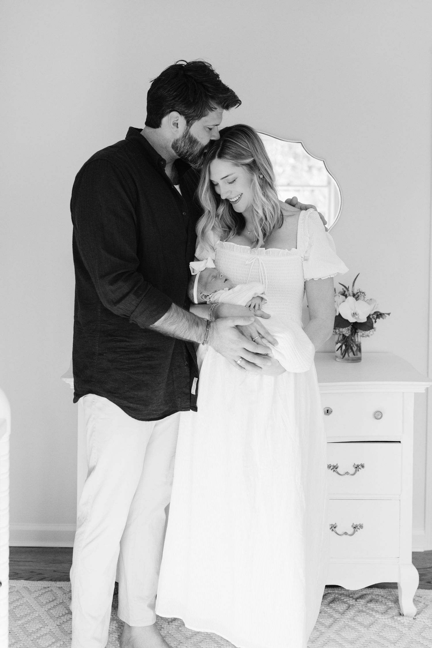 Black and white photos of a couple sharing tender moments near a white dresser.