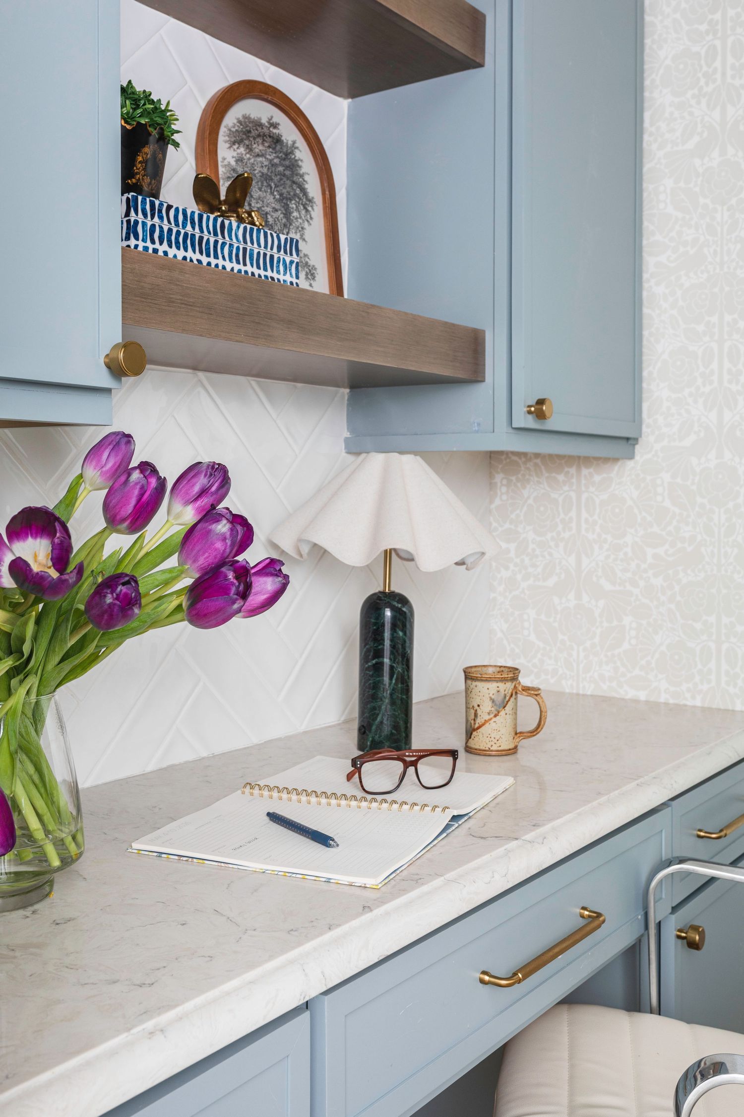Modern kitchen with light blue cabinets, marble countertops, and purple tulips in a vase displayed on the counter.