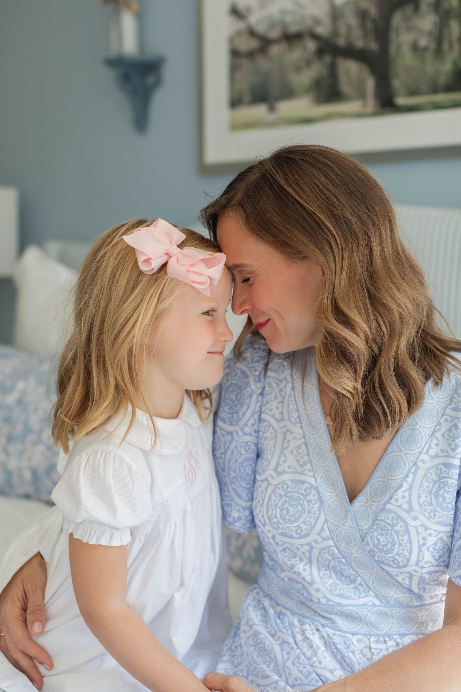 Sweet candid moments captured between a parent and child sitting together on a blue and white floral bed.