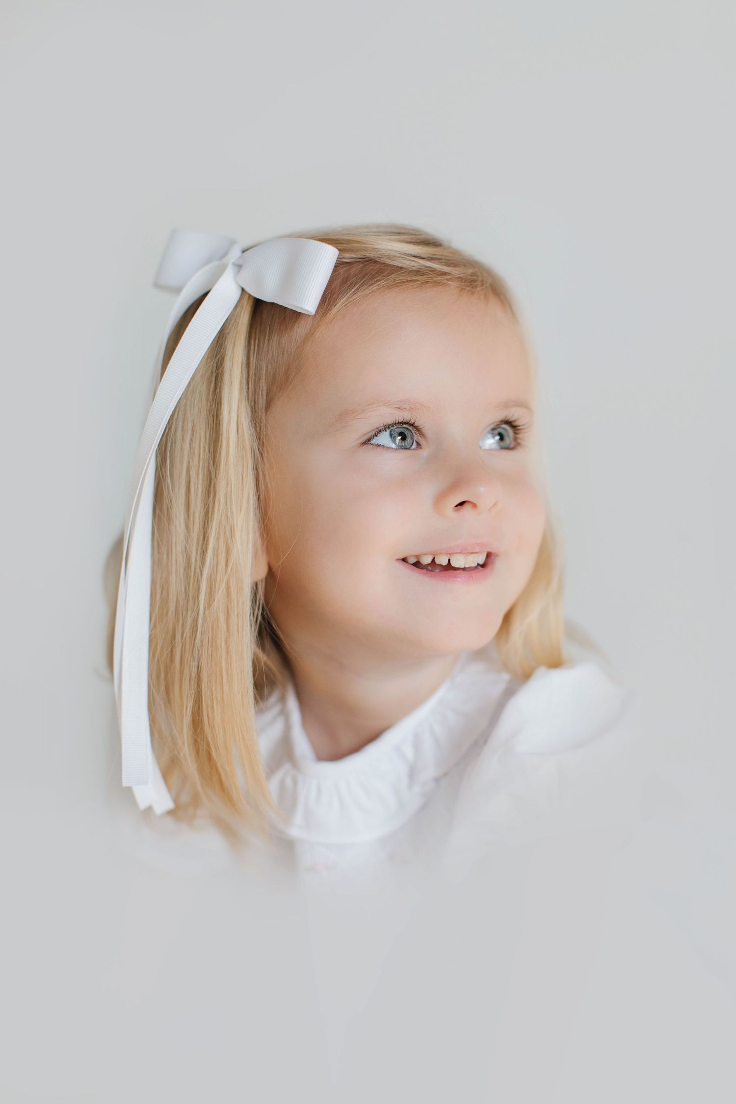 A series of dreamy white photographs showing a child with blonde hair and white bow looking upward with different expressions.