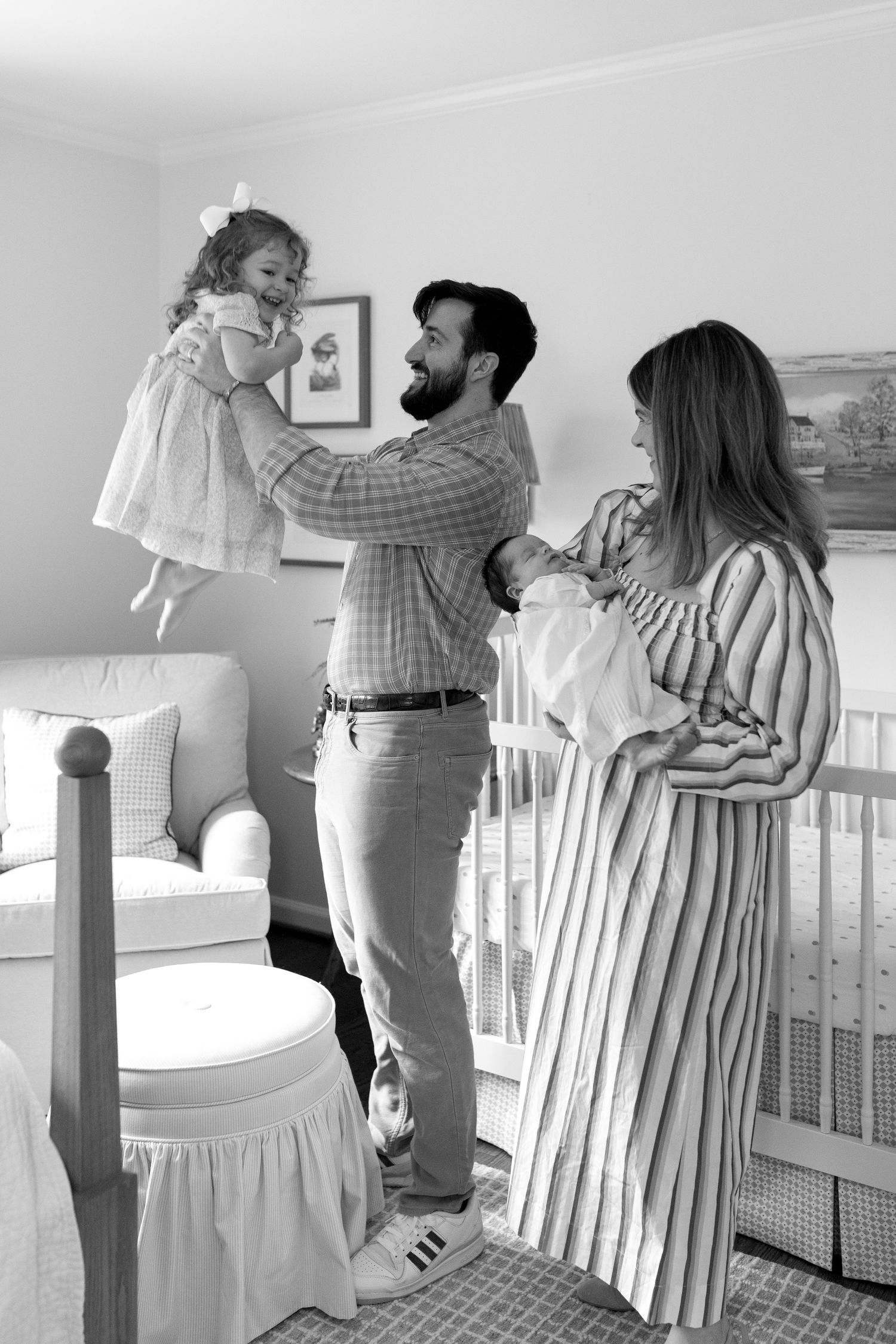 Black and white photo of a family sharing a tender moment together in a nursery with white decor and furniture.
