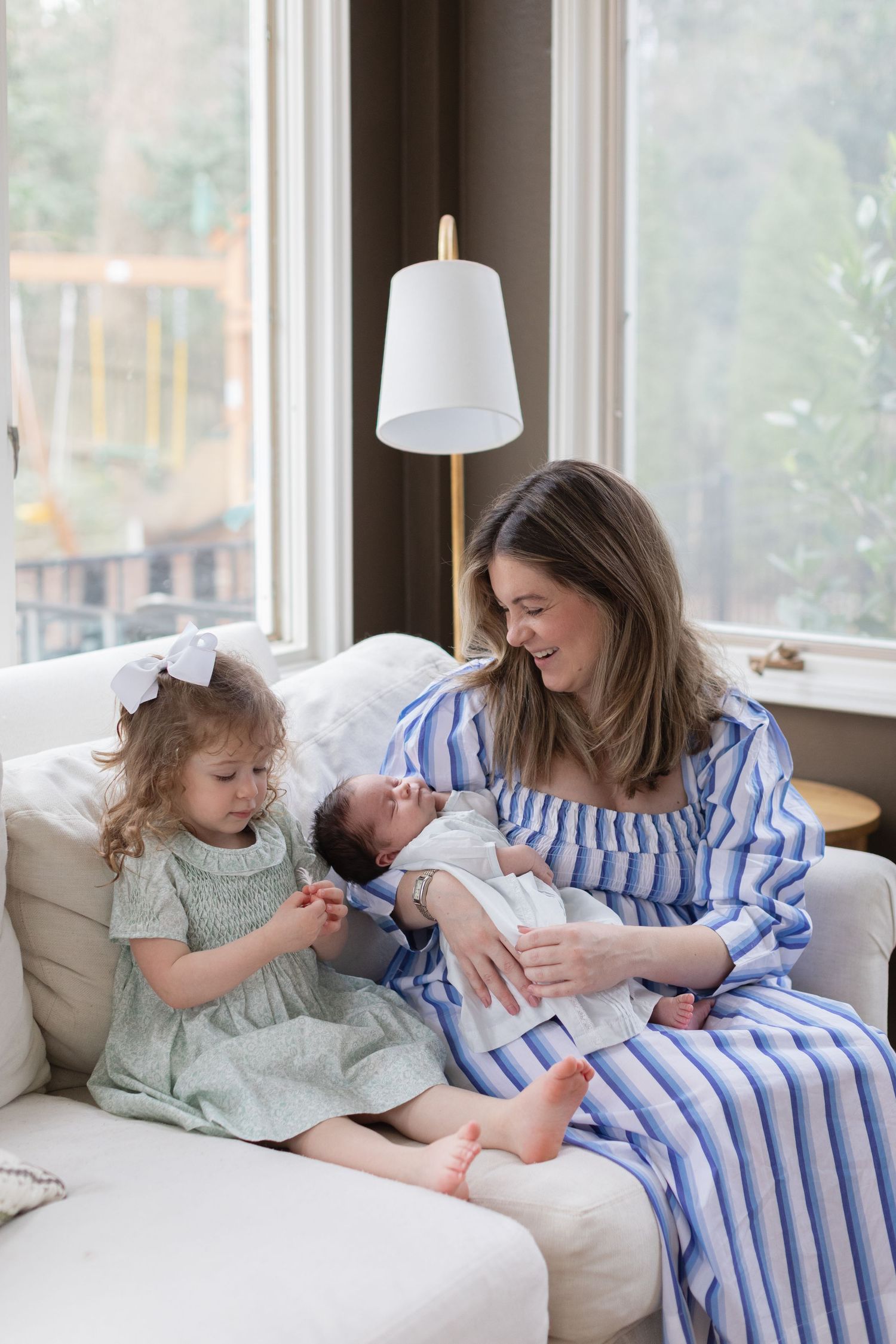 A family scene on a couch by windows showing loving interactions with a newborn baby.
