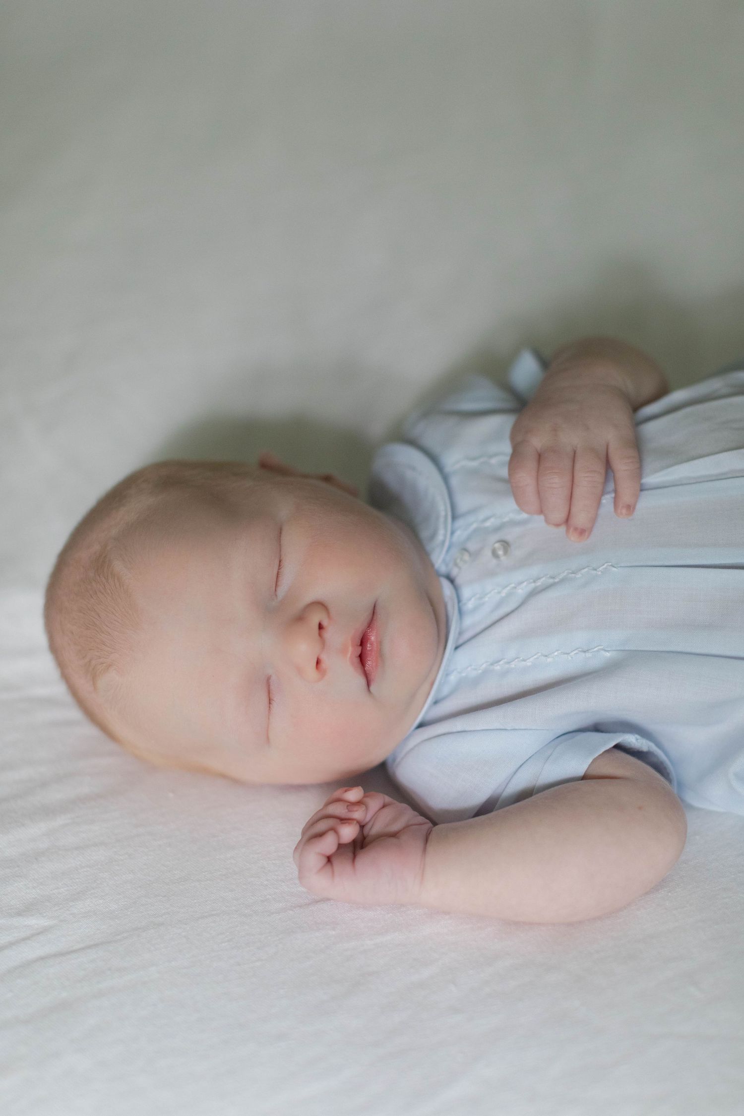 A peaceful scene of a sleeping infant in a white onesie resting on crisp white bedding.