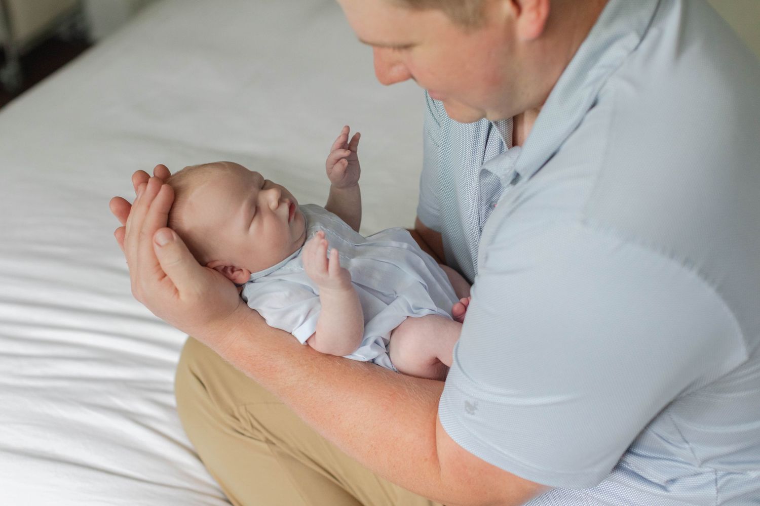 A tender parenting moment showing gentle interaction with a lying baby dressed in light colored clothing.