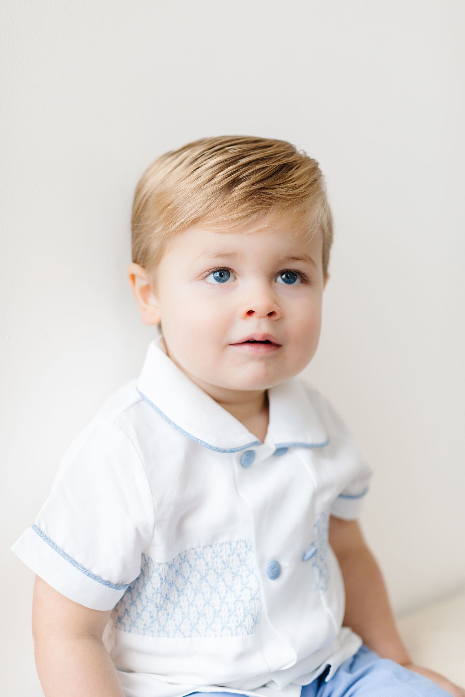 Young child wearing a white collared shirt with blue trim sits against light background.