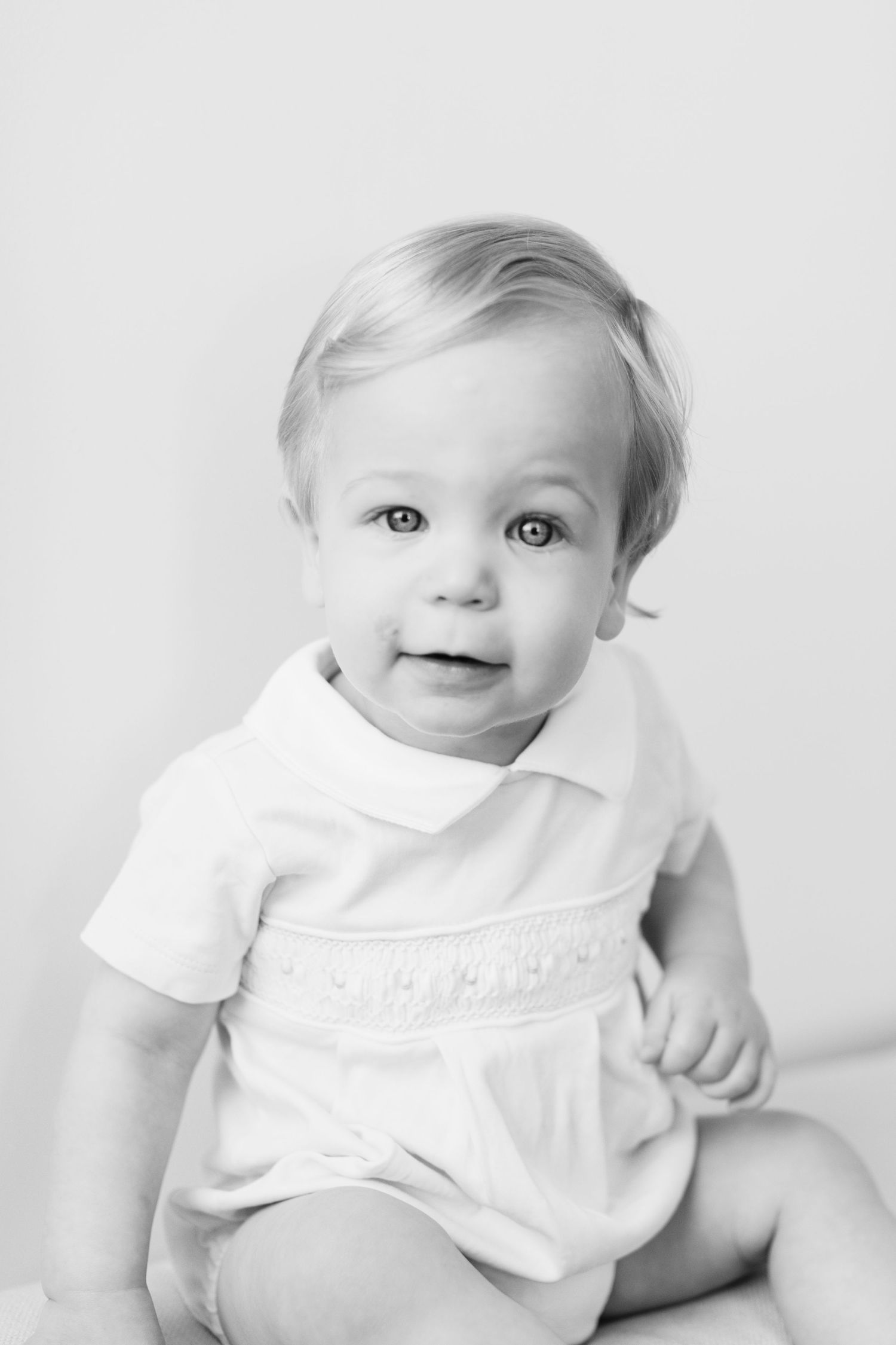 Adorable baby in white outfit poses on light background showing various expressions in photo series.