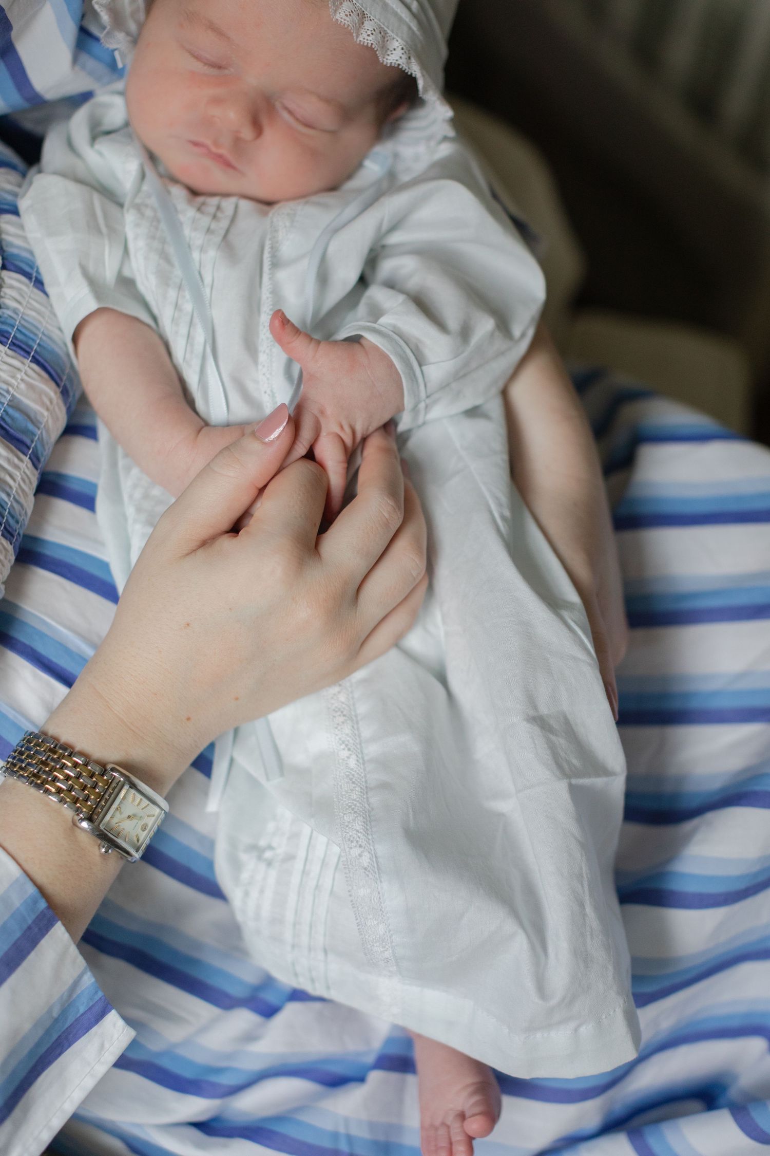 Close-up shots of baby wearing white christening gown with blue and white striped details.