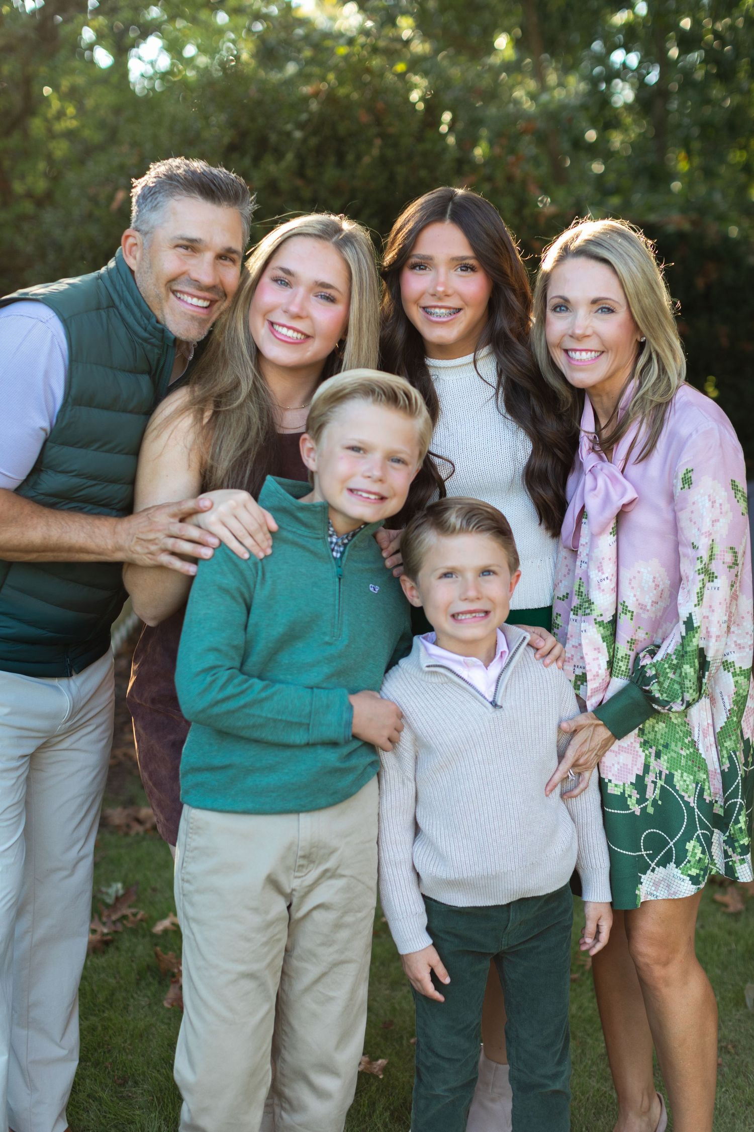 A family wearing coordinated green and white outfits poses together outdoors for casual portraits in a garden setting.