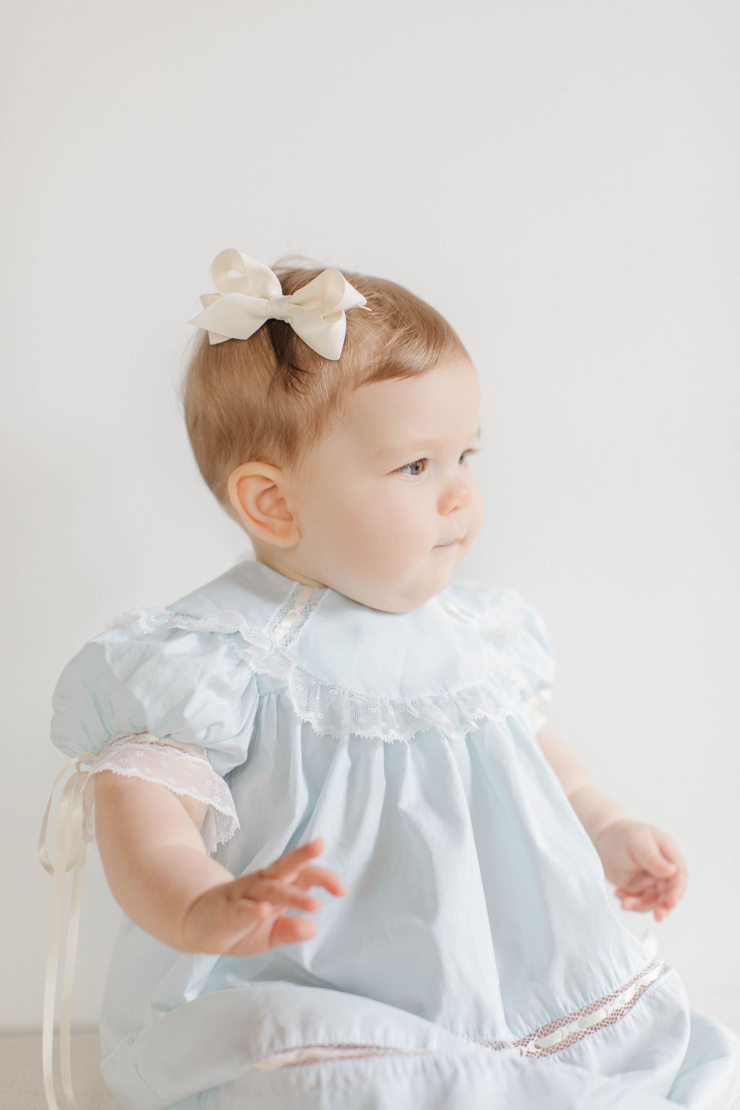 Toddler wearing a light blue vintage-style dress with white lace collar and cream bow hair accessory.