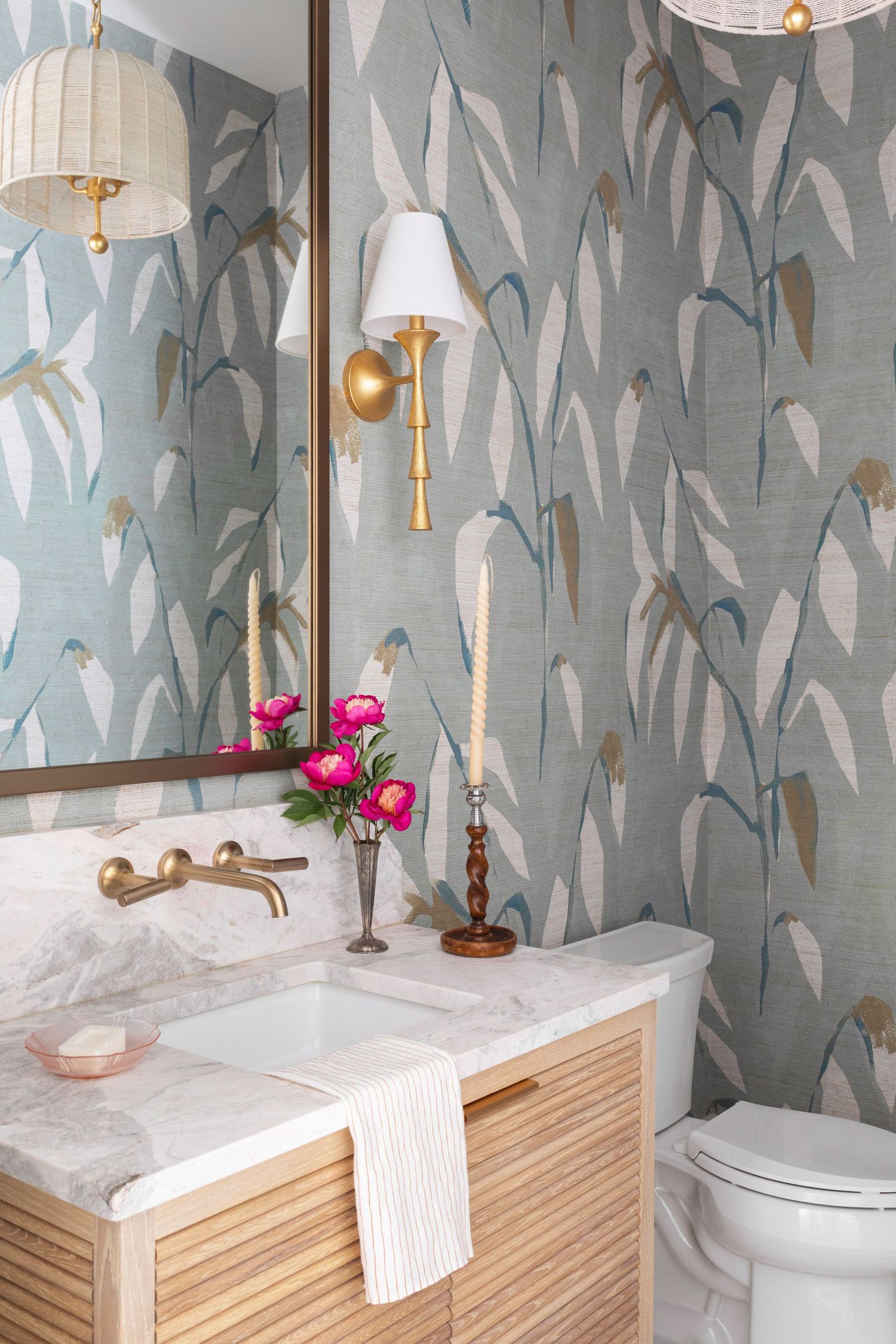 Elegant powder room with botanical wallpaper, marble vanity, wood cabinet, brass fixtures, and pink peonies accents.