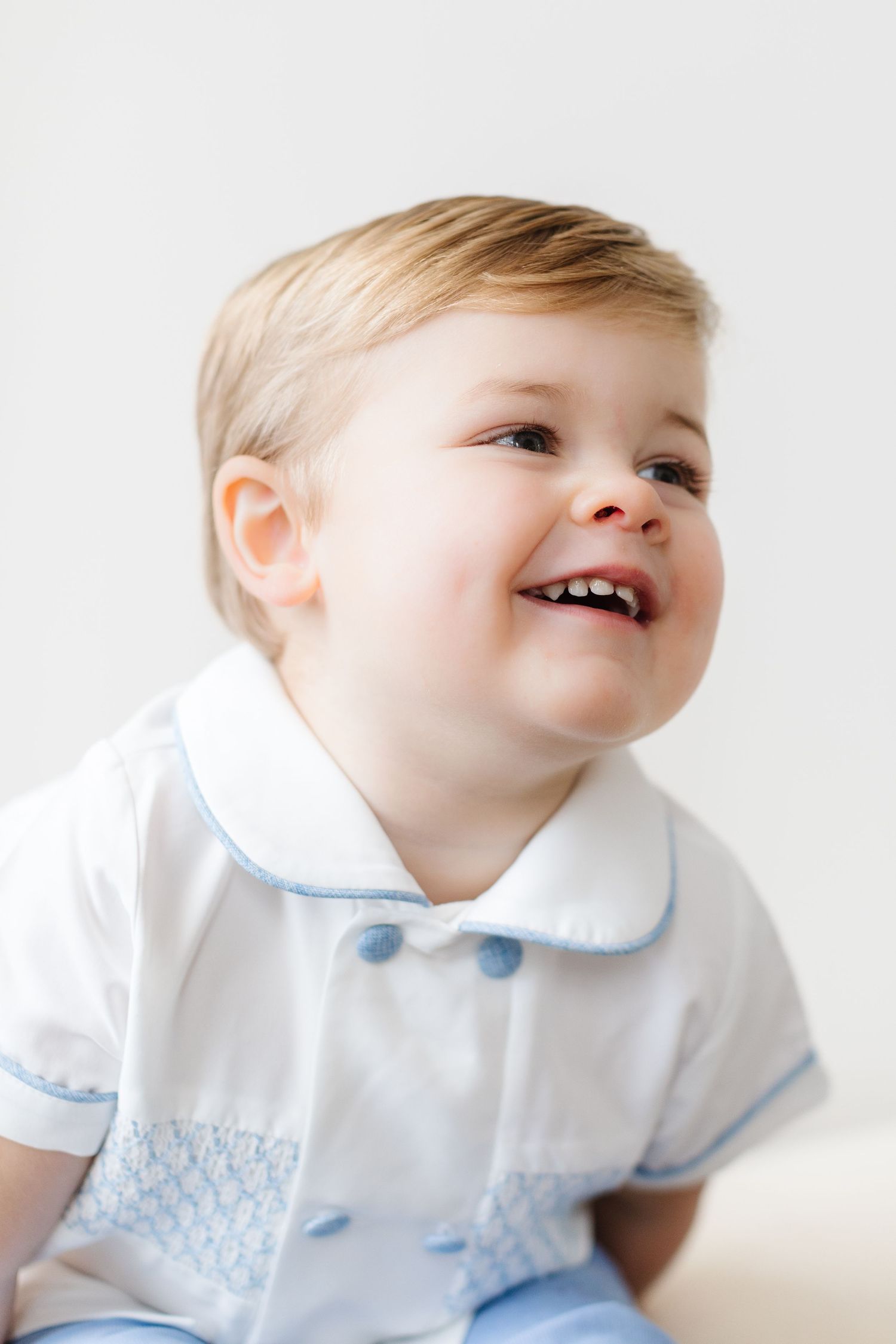 A young child in a white collared outfit smiles and looks up in a series of four connected photos.
