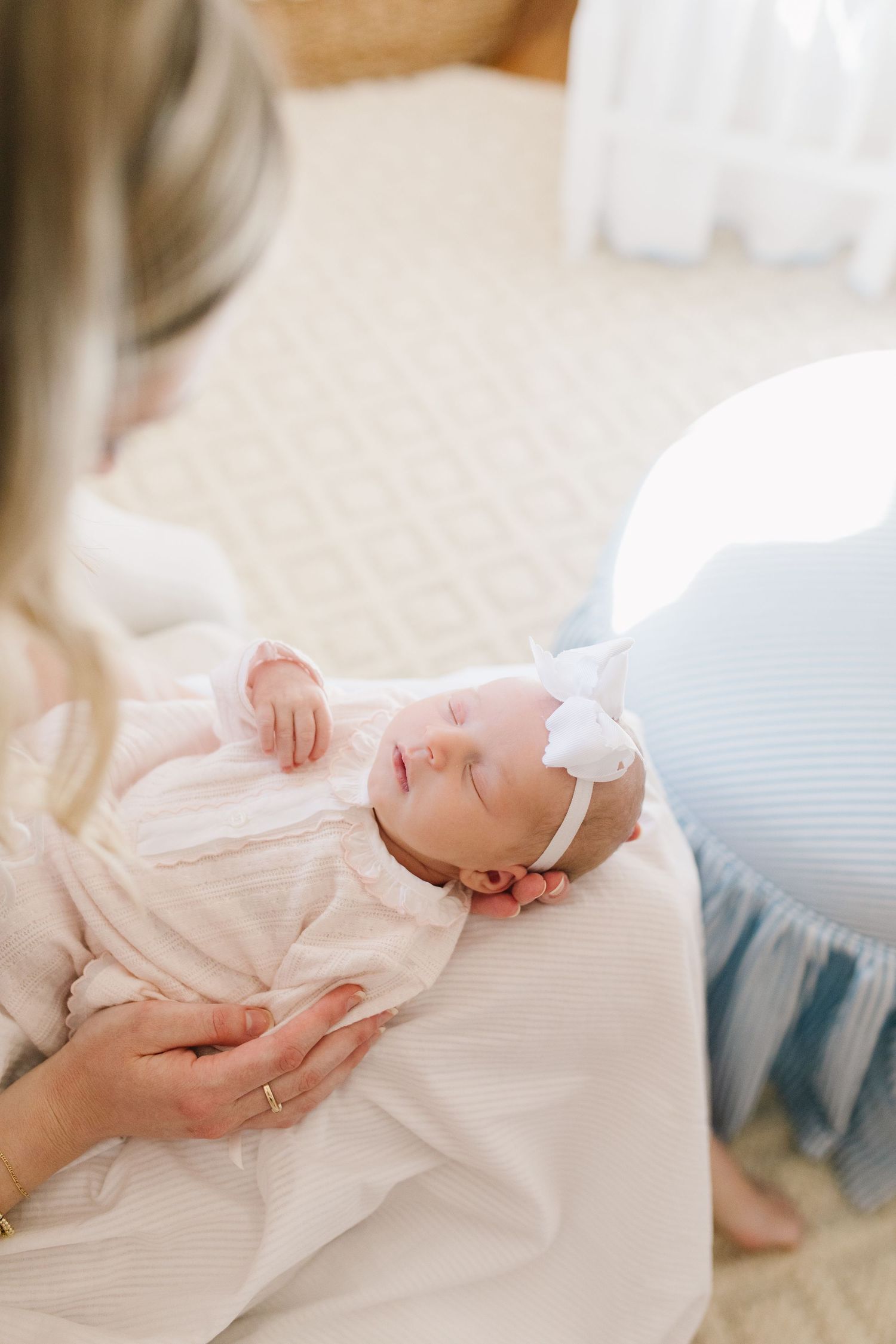 Newborn baby in white outfit resting on soft surface while being cradled.