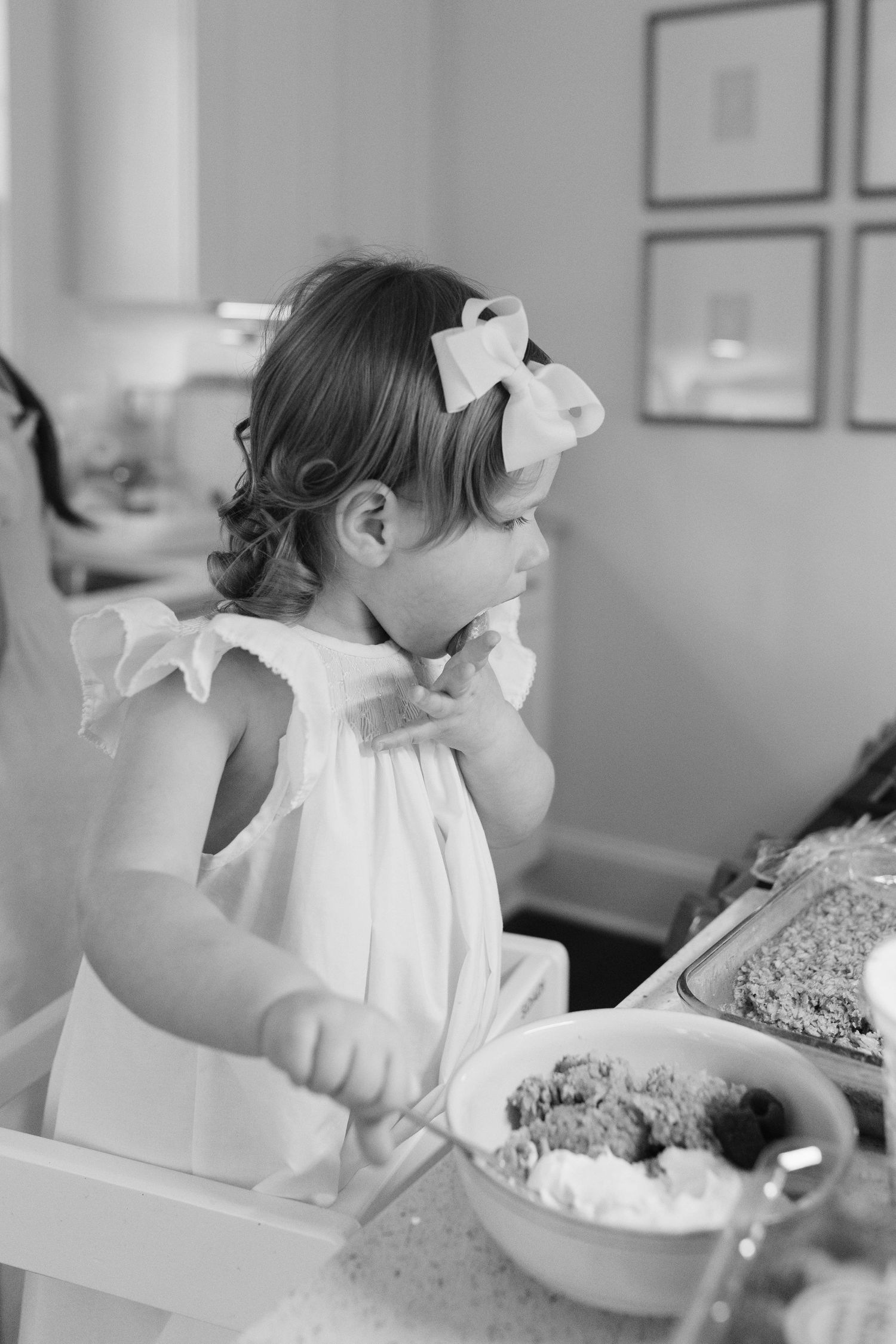 Child in white dress sitting at table in black and white photography.